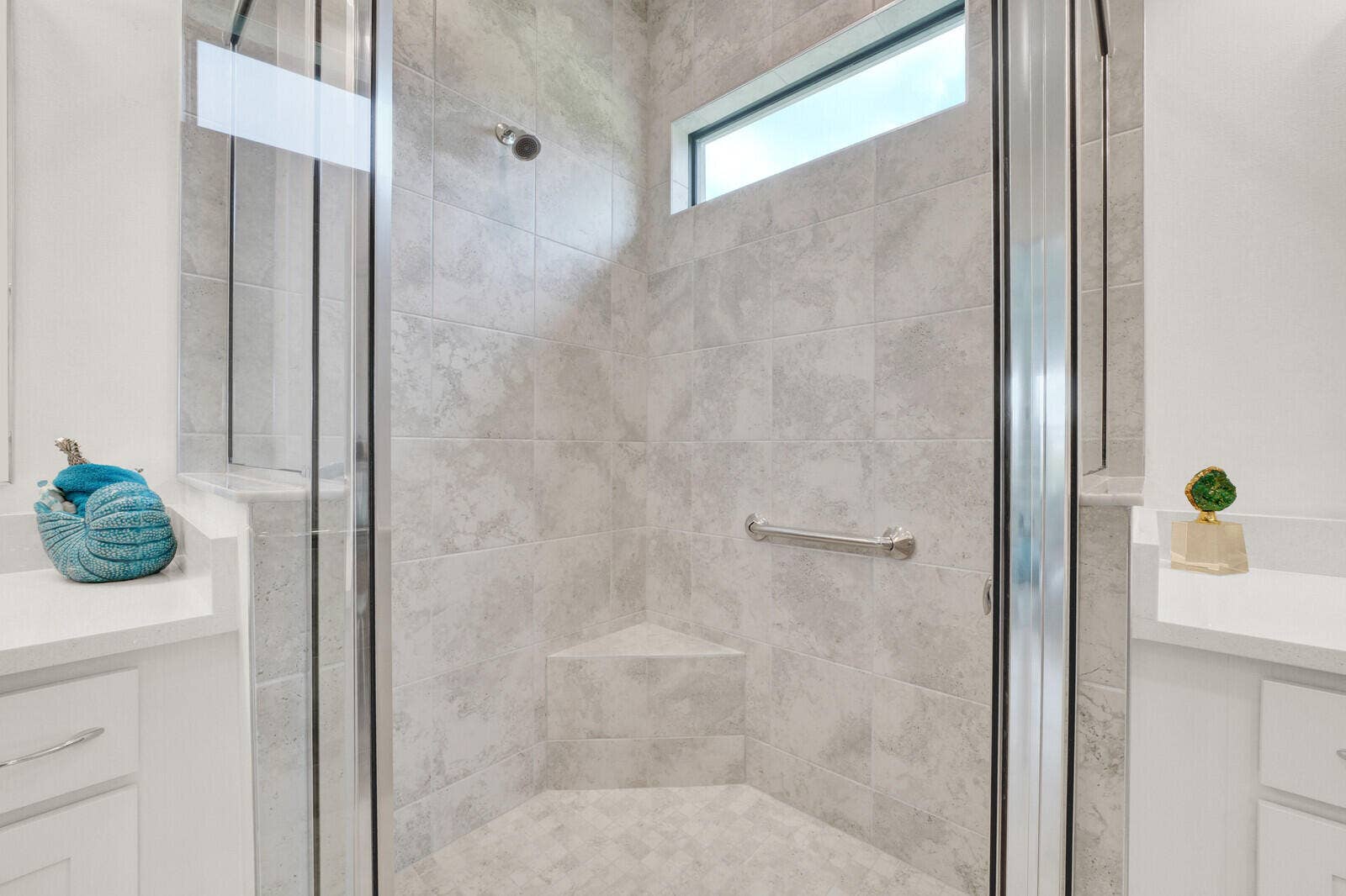 Glass-enclosed shower featuring gray large-format tile, corner bench seating, a fixed shower head, and a transom window