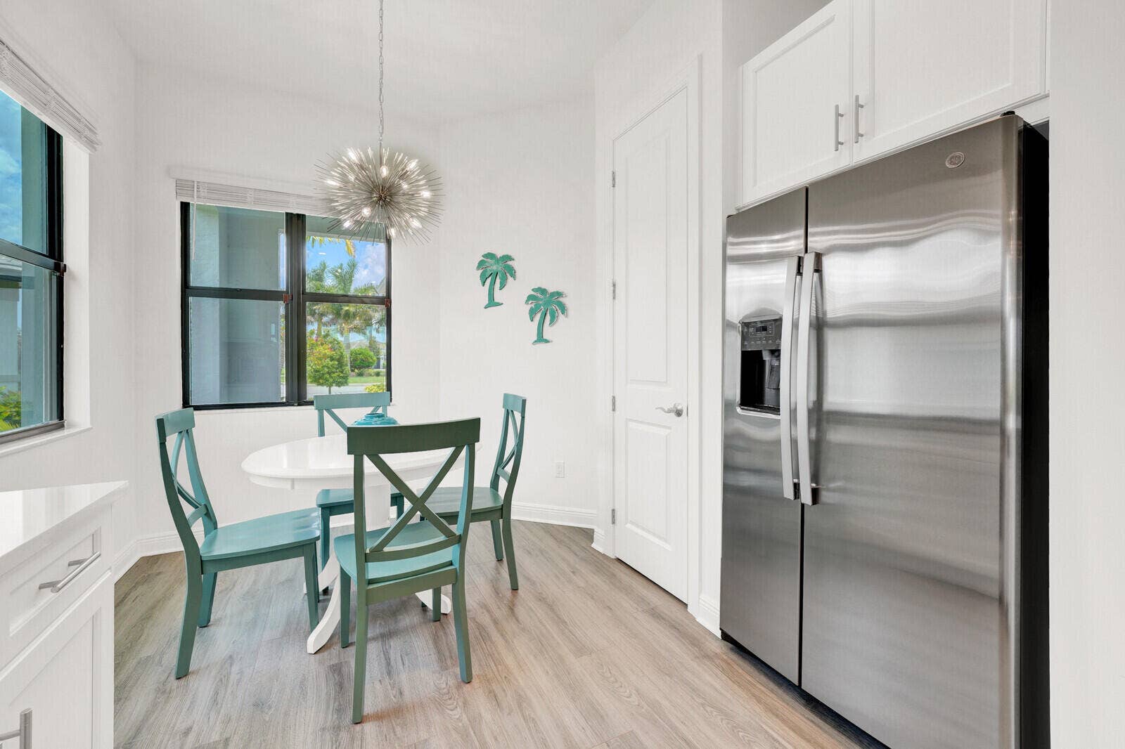 Contemporary dining nook featuring a modern sputnik-style chandelier, expansive windows, wood-finish flooring, and a stainless steel side-by-side refrigerator