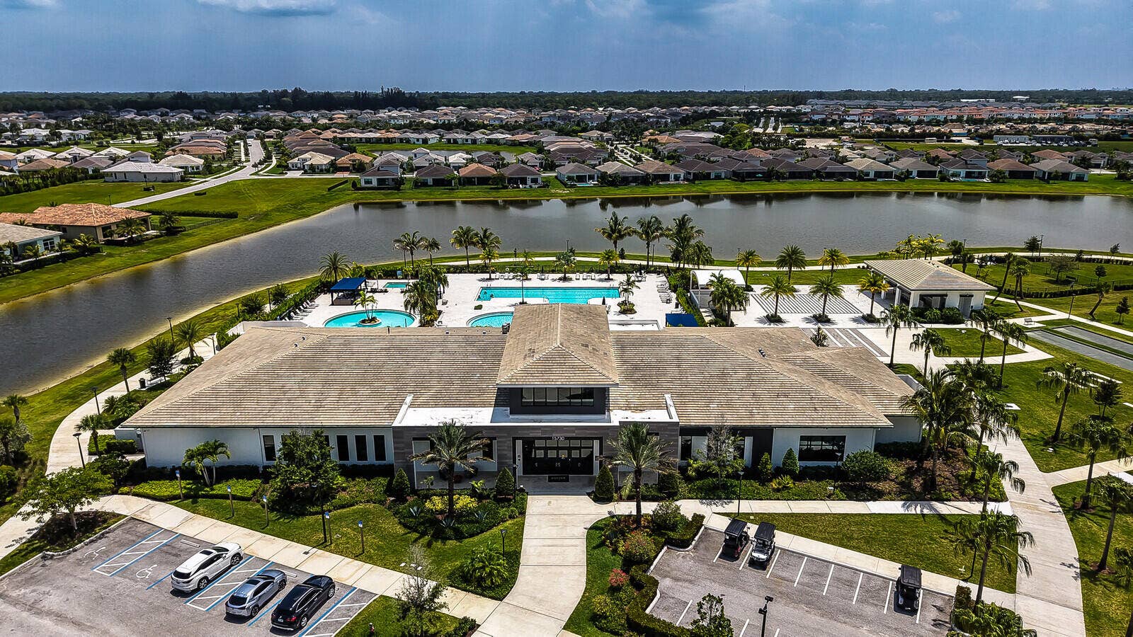 Community amenity building with multiple swimming pools, extensive patio space, and surrounding palm trees