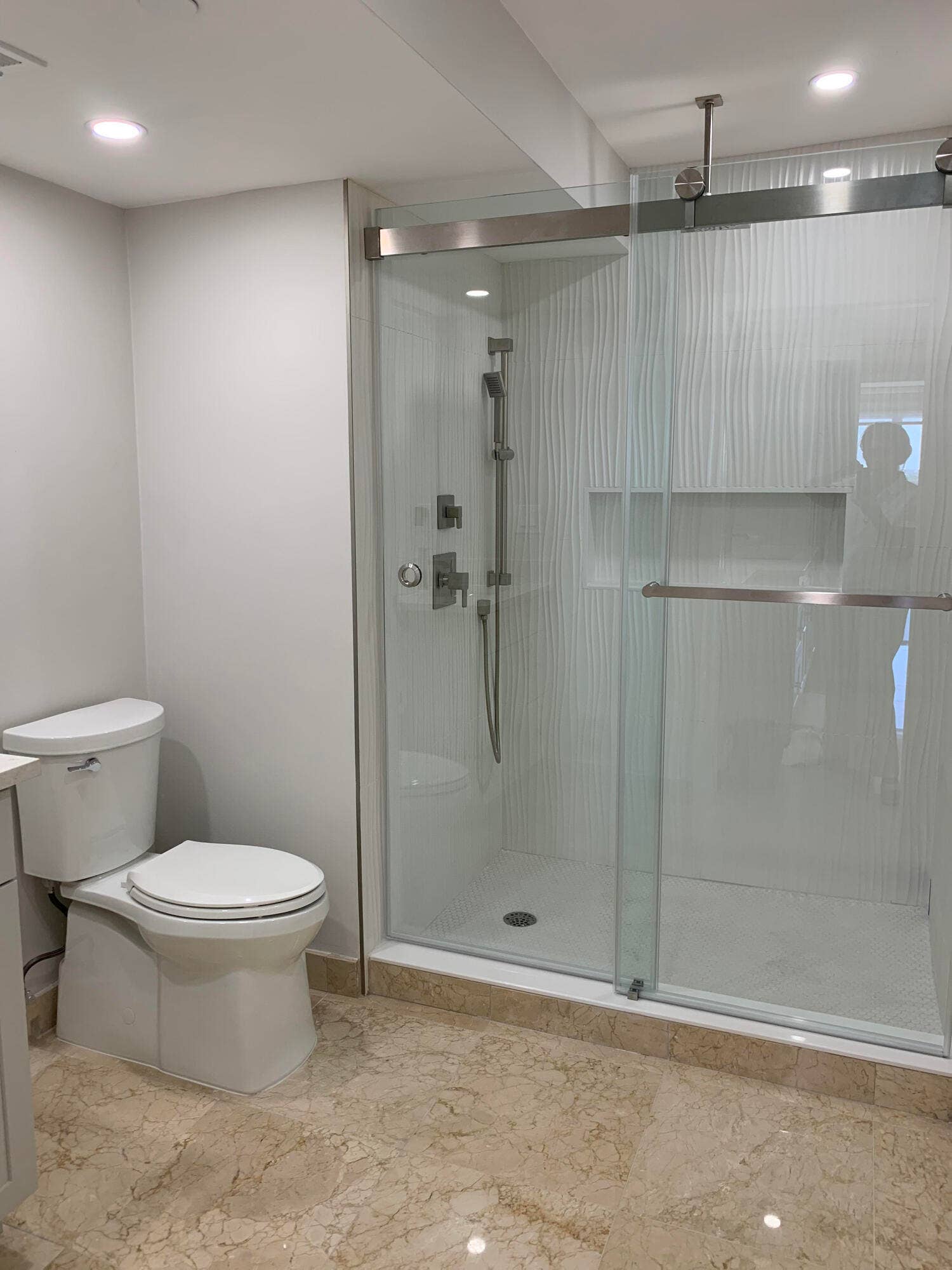 3115 S Ocean Boulevard, #1002, Highland Beach, FL 33487 Modern bathroom featuring a frameless glass shower enclosure with a sliding door, textured shower wall tile, recessed shower niche, and a rain shower head with an additional hand-held sprayer