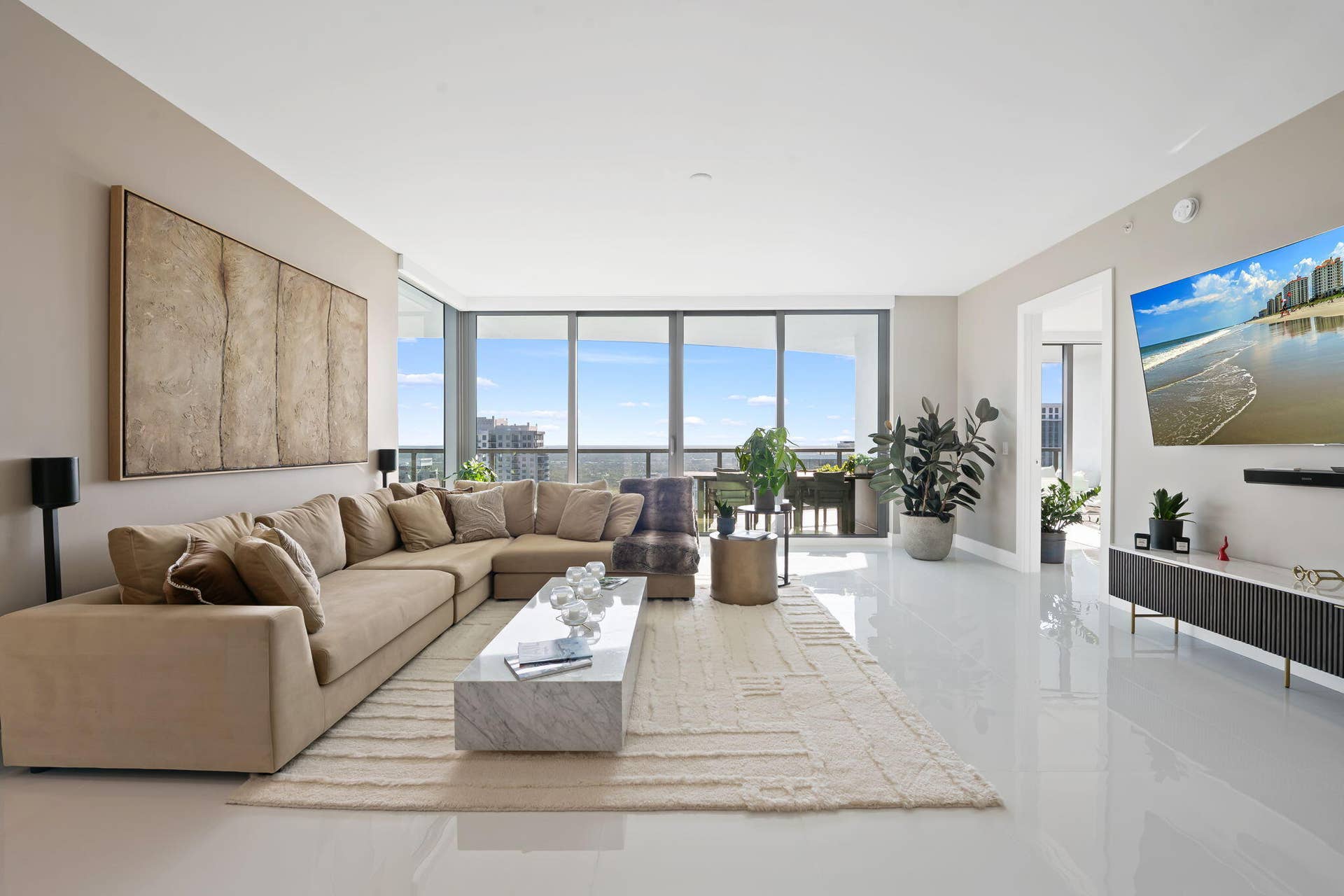 100 E Las Olas Boulevard, #3804, Fort Lauderdale, FL 33301 Open-concept living area with expansive floor-to-ceiling windows, showcasing a contemporary white flooring, a built-in entertainment console, and a large doorway