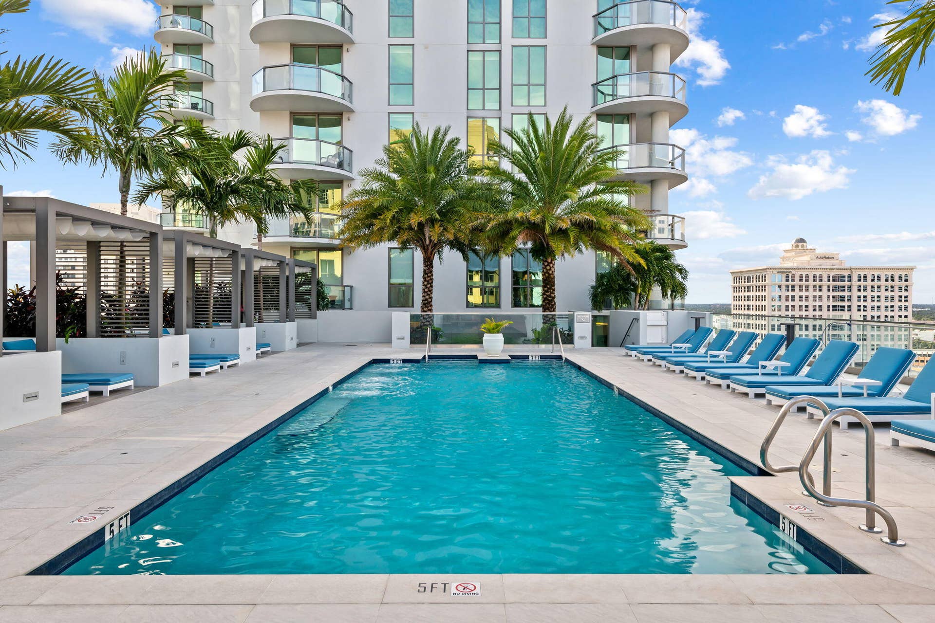 100 E Las Olas Boulevard, #3804, Fort Lauderdale, FL 33301 Resort-style pool area featuring ample lounge seating, private cabanas, and mature palm trees, set against a backdrop of a modern high-rise building with curved glass balconies