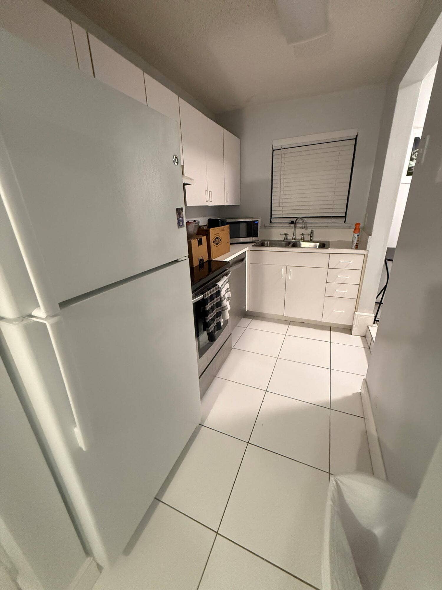 4121 NE 21st Terrace, #3, Lighthouse Point, FL 33064 Compact kitchen featuring white cabinetry, white tile flooring, stainless steel range, and a window with blinds