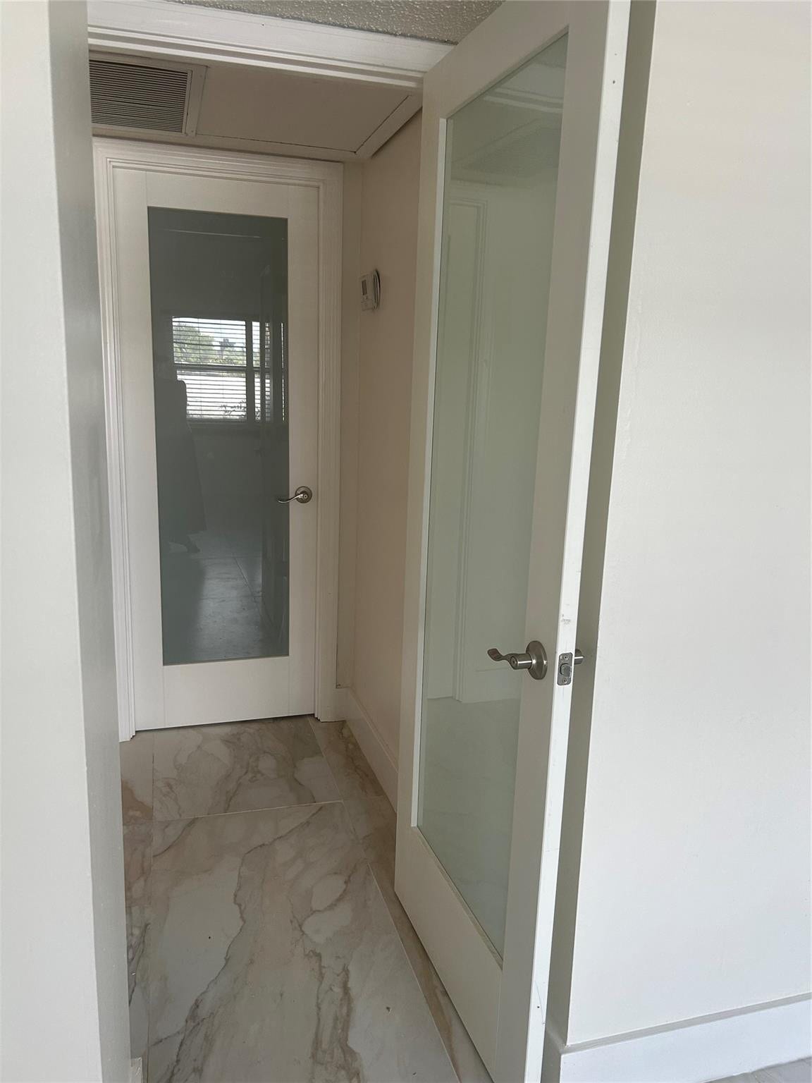 550 Bayshore Drive, #102, Fort Lauderdale, FL 33304 Hallway off the living room where entrance to bedroom and bathroom are separated by frosted glass doors. Th New air-conditioning vent covers are throughout the unit of which one is attached to the ceiling.