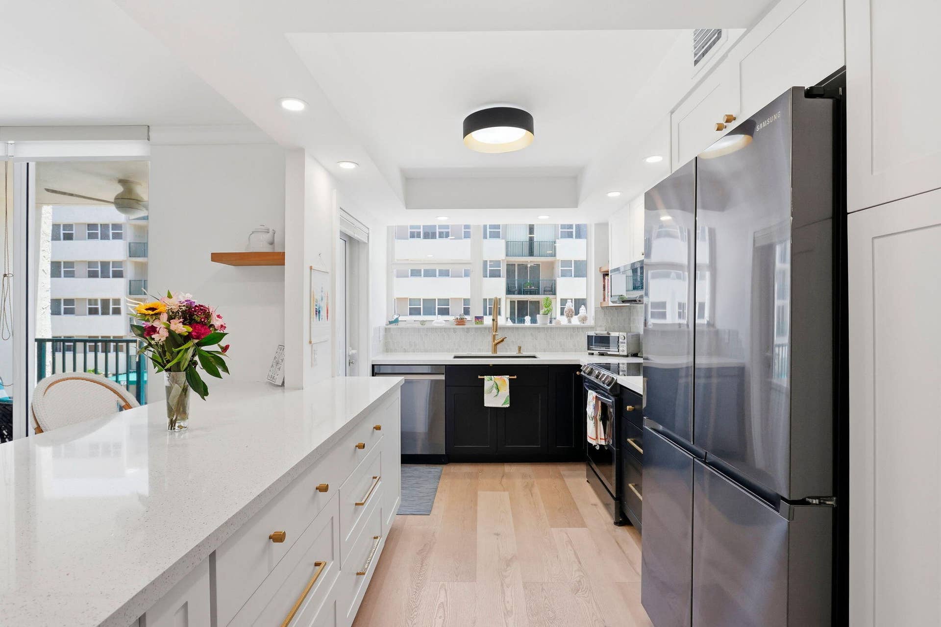 1239 Hillsboro Mile, #302, Hillsboro Beach, FL 33062 Modern kitchen featuring a large white quartz countertop island with gold-finish hardware, stainless steel appliances, light wood-finish flooring, and white and black cabinetry