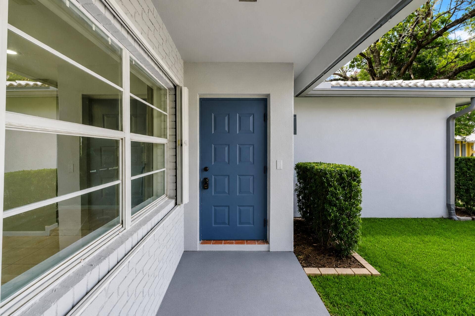 3843 NW 81st Terrace, Coral Springs, Coral Springs, FL 33065 Entryway featuring a paneled blue door, large multi-pane windows, white brick siding, and a covered porch
