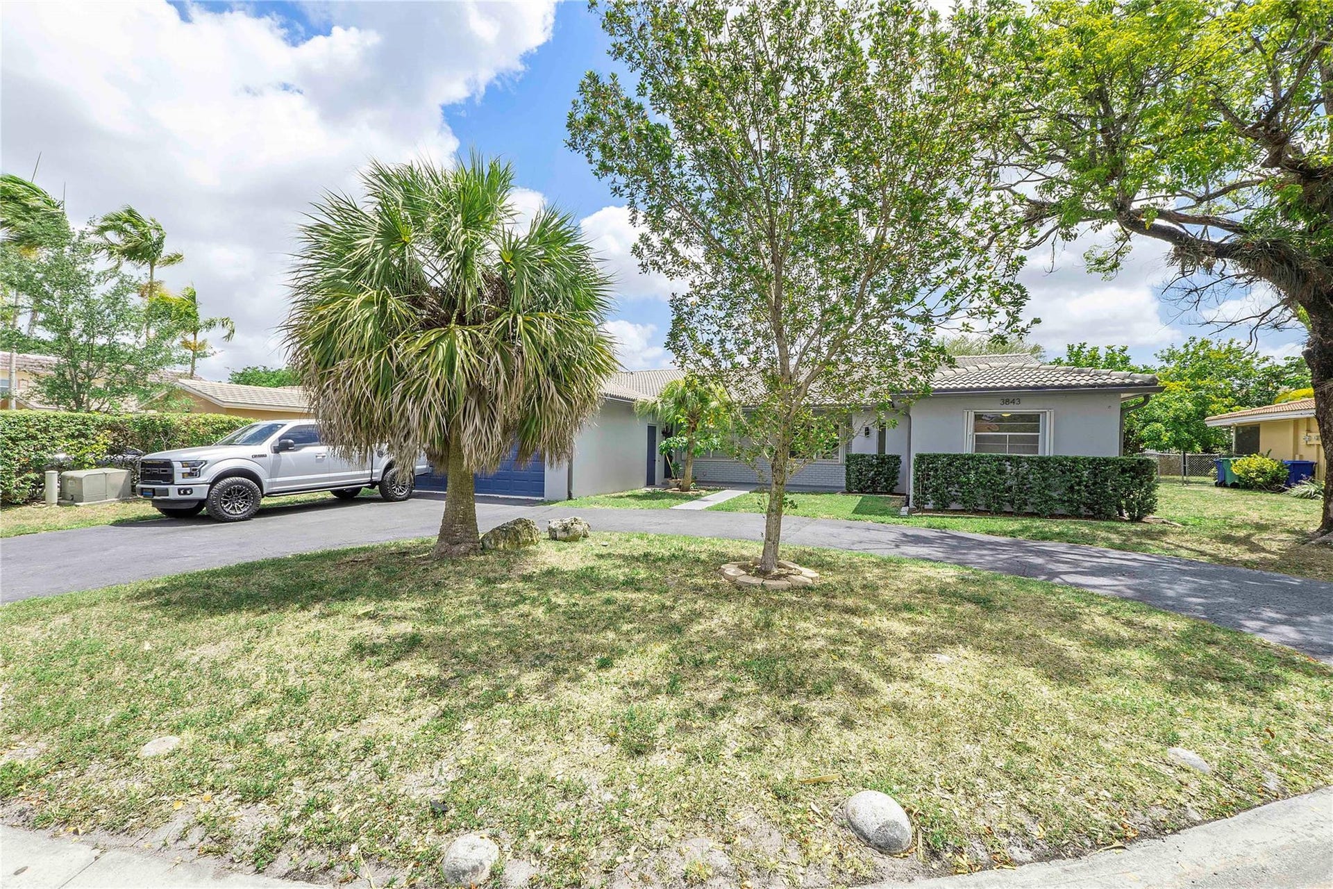 3843 NW 81st Terrace, Coral Springs, Coral Springs, FL 33065 Front exterior featuring mature trees, established landscaping, a driveway, and a partially visible garage