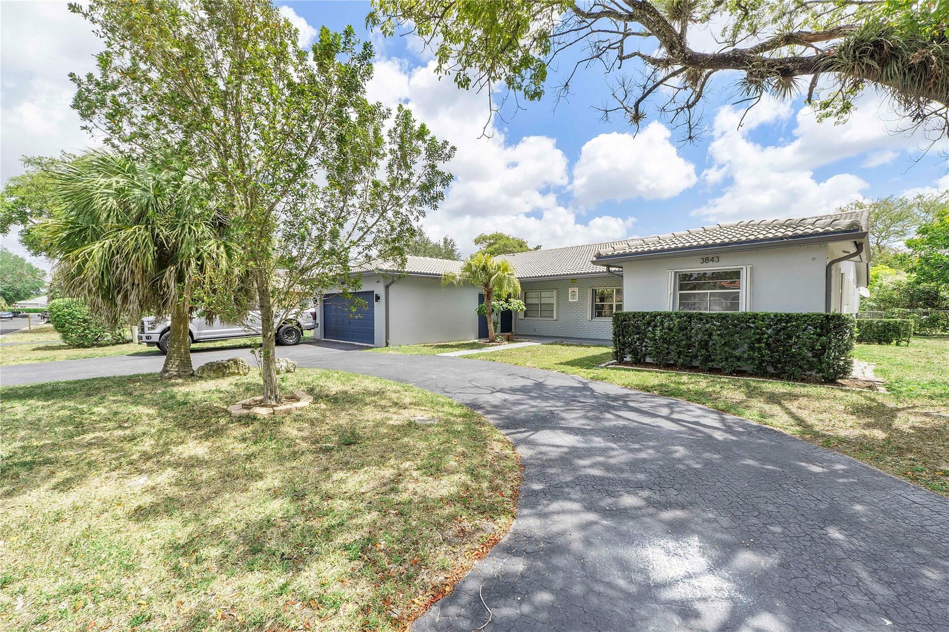 3843 NW 81st Terrace, Coral Springs, Coral Springs, FL 33065 Contemporary stucco exterior with a tiled roof, mature tropical landscaping, a paved driveway, and an attached garage with a blue door
