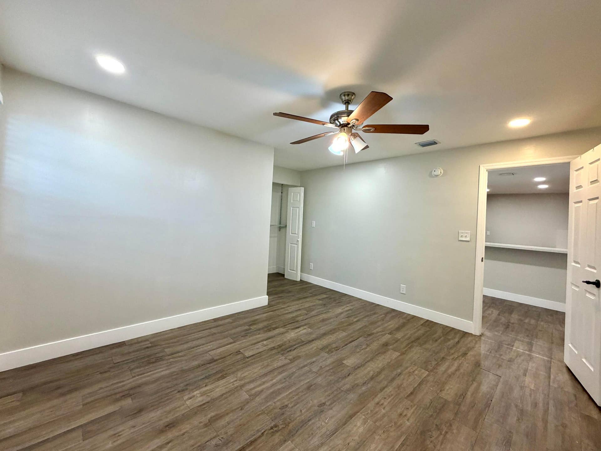 Spacious interior room featuring wood-style laminate flooring, recessed lighting, and a ceiling fan with light fixture