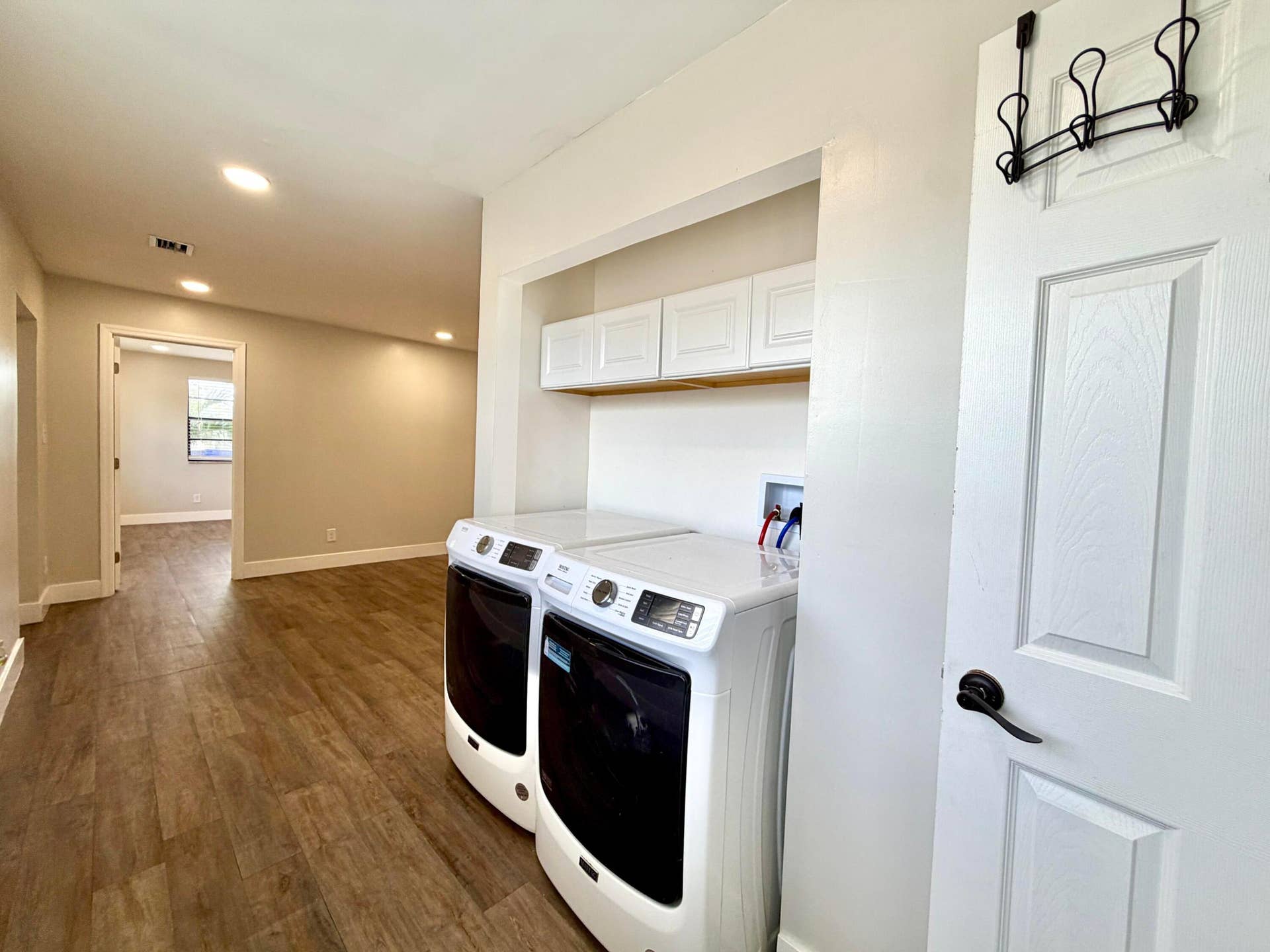 Dedicated laundry area featuring upper white cabinetry, a built-in shelf, and wood-style laminate flooring