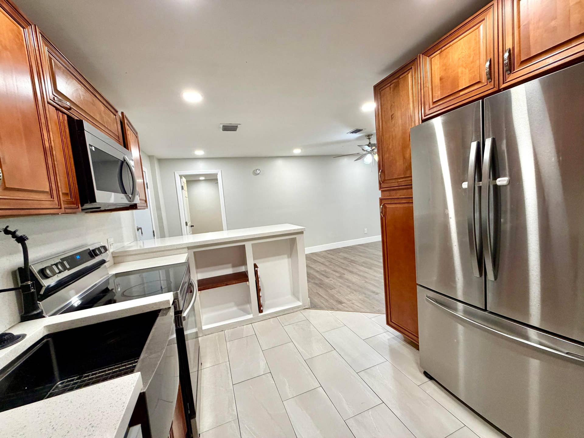 Kitchen featuring wood cabinetry, stainless steel appliances, white countertops, premium tile flooring, and a built-in breakfast bar with open shelving