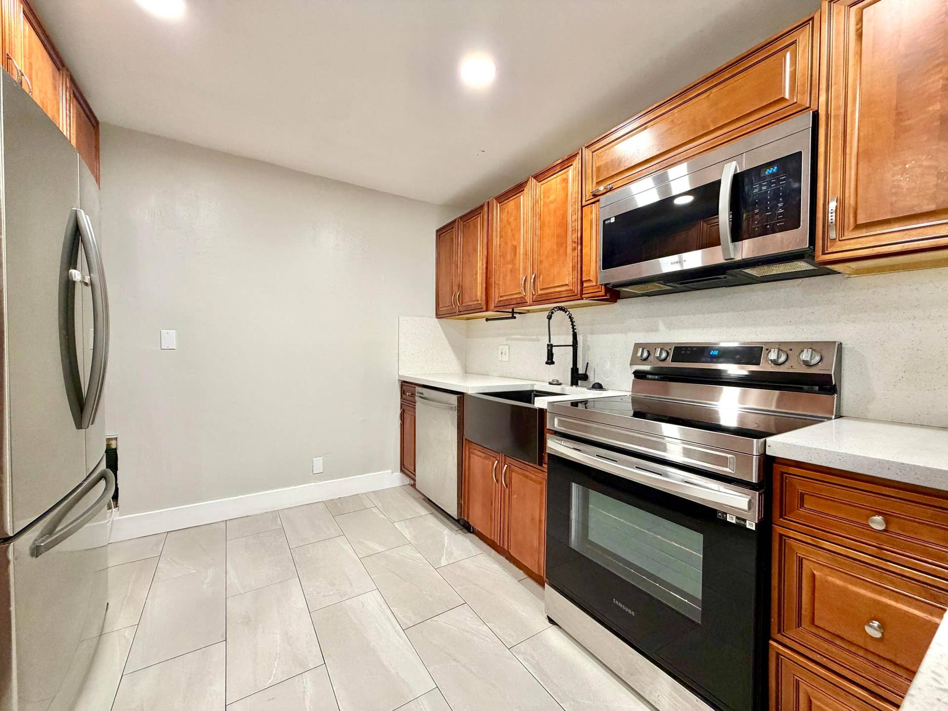 Kitchen featuring wood cabinetry, stainless steel appliances, white countertops, and premium light-toned tile flooring