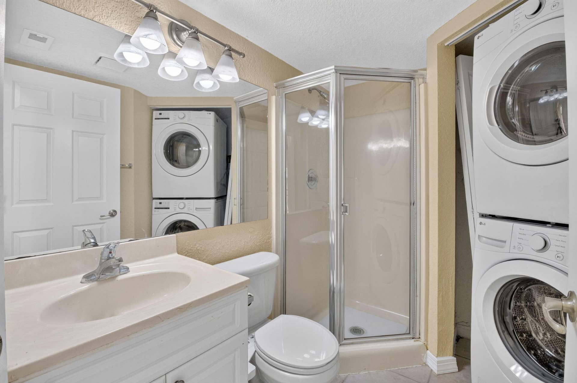 8230 Severn Drive, #A, Boca Raton, FL 33433 Bathroom featuring a compact shower enclosure with a clear glass door, a vanity with an integrated sink and light-toned countertop, a white toilet, and a stacked washer and dryer unit