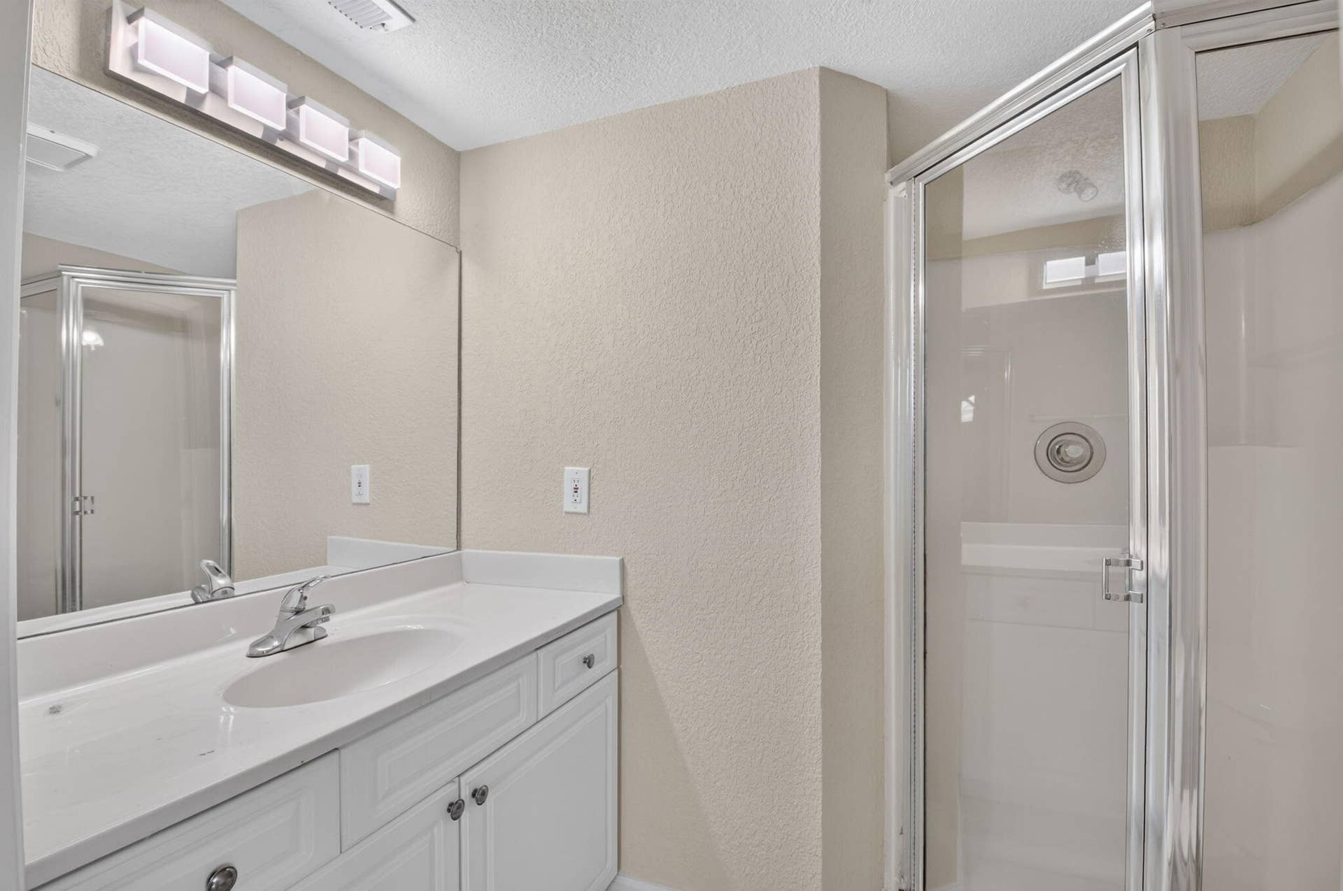 8230 Severn Drive, #A, Boca Raton, FL 33433 Bathroom featuring a glass-enclosed shower, white vanity with integrated sink, chrome faucet, and expansive wall mirror with a four-bulb light fixture
