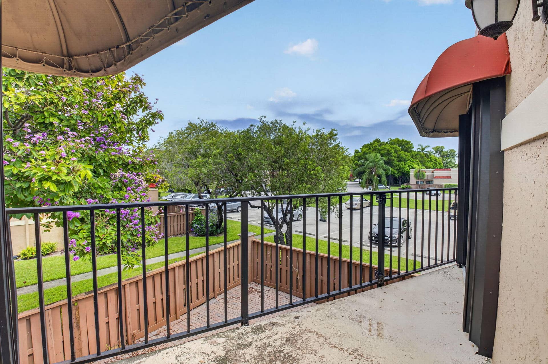 8230 Severn Drive, #A, Boca Raton, FL 33433 Balcony with a black metal railing and concrete flooring, featuring a red awning and an exterior wall light fixture