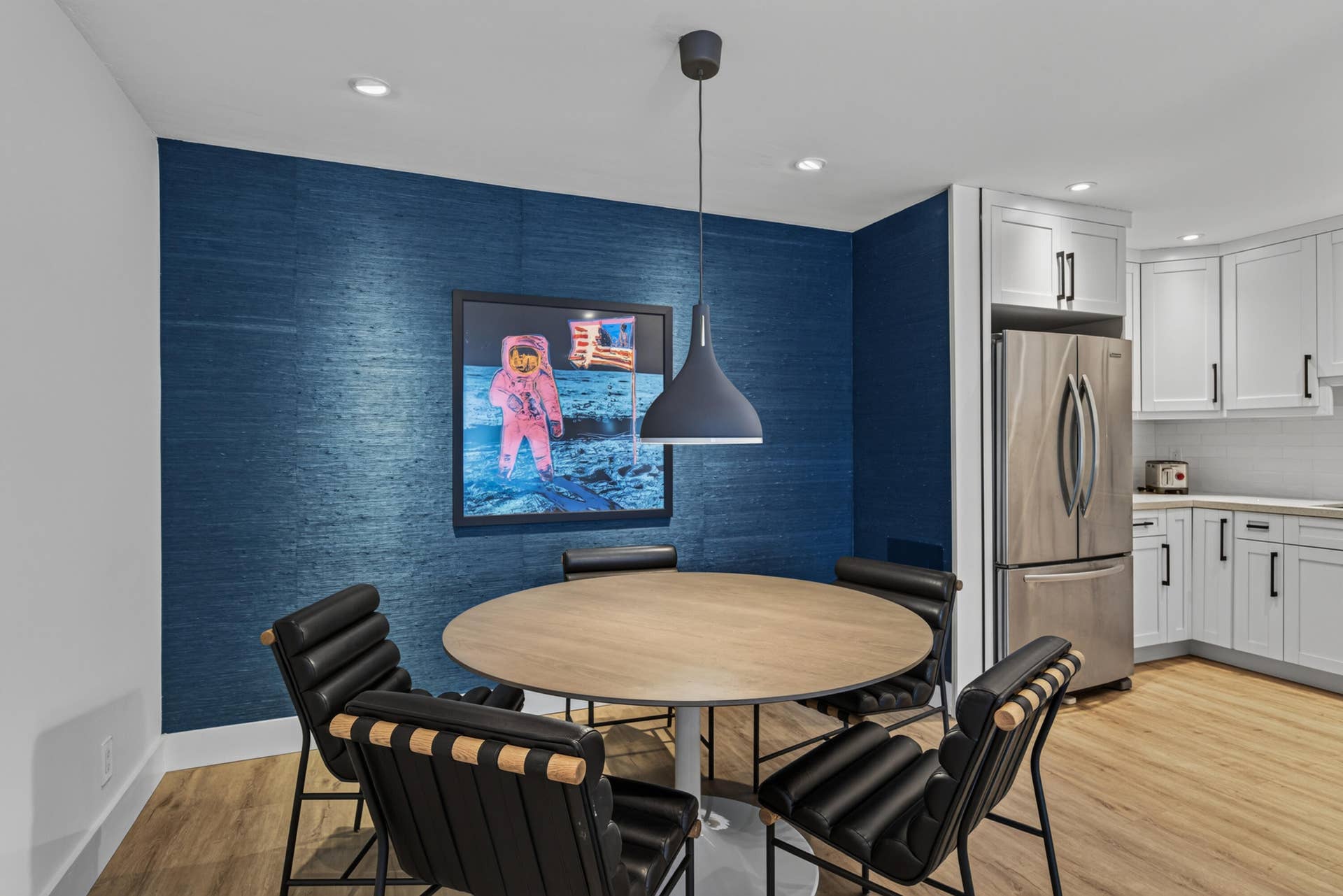 Dining area featuring wood-finish flooring, a contemporary pendant light fixture, recessed ceiling lighting, and an accent wall with blue textured wallcovering.