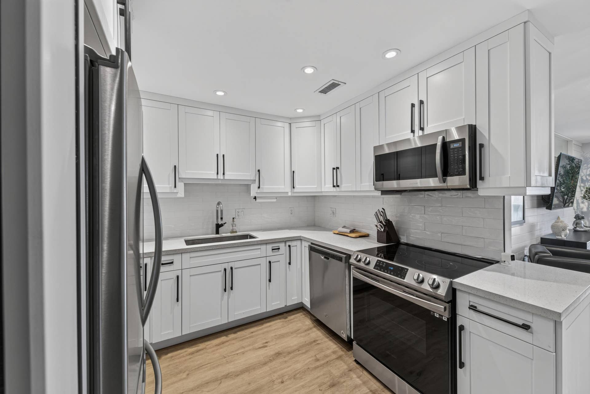 Kitchen featuring white shaker cabinetry with matte black hardware, stainless steel appliances, light-toned countertops, and a white subway tile backsplash