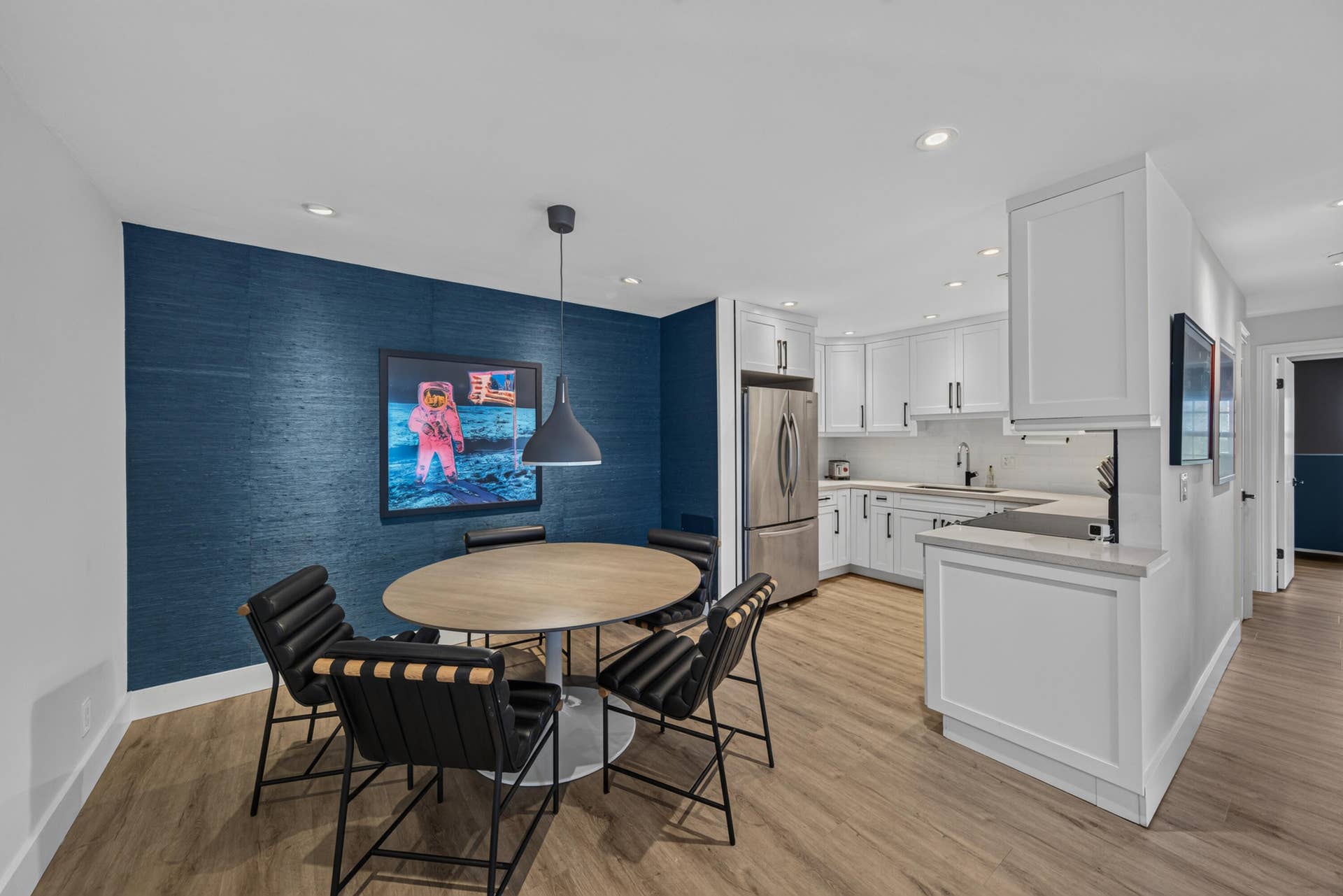 Open-concept kitchen and dining area featuring wood-finish flooring, recessed lighting, white shaker cabinetry, stainless steel appliances, and a blue textured accent wall