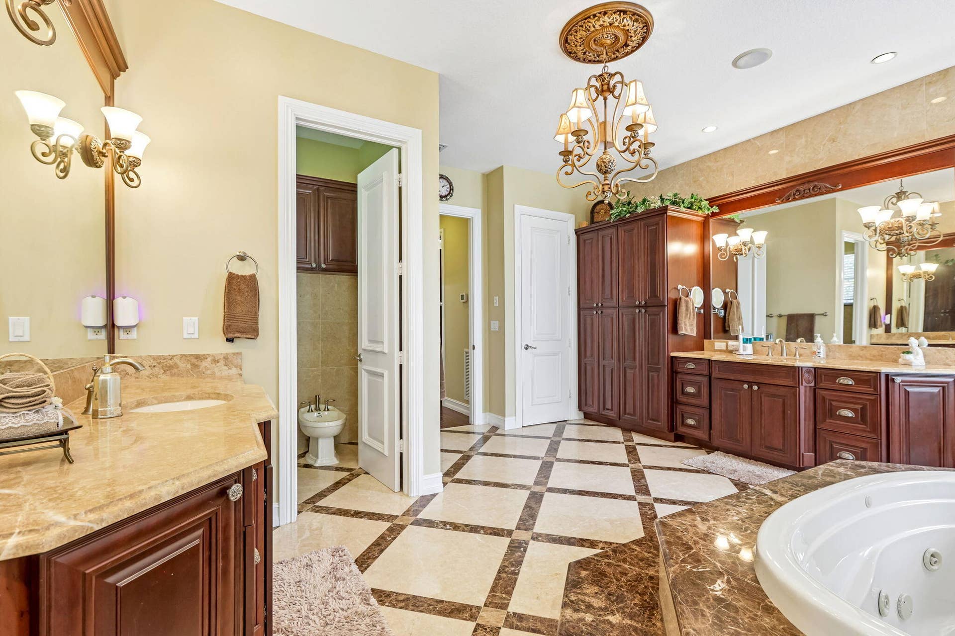 Expansive bathroom featuring a checkerboard tile floor, a recessed jetted tub with a stone surround, and dual vanity areas with stone countertops and wood cabinetry