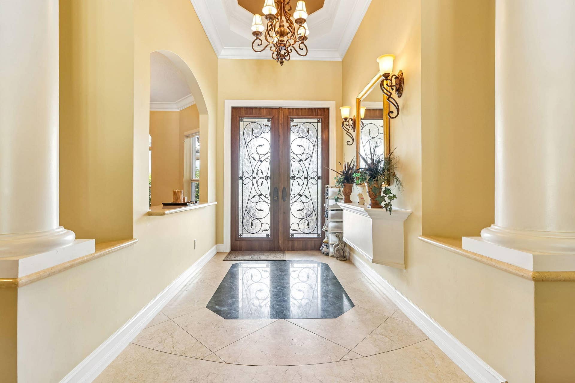 Entry foyer featuring double wooden doors with decorative glass inserts, a coffered ceiling with a chandelier, and sconce lighting