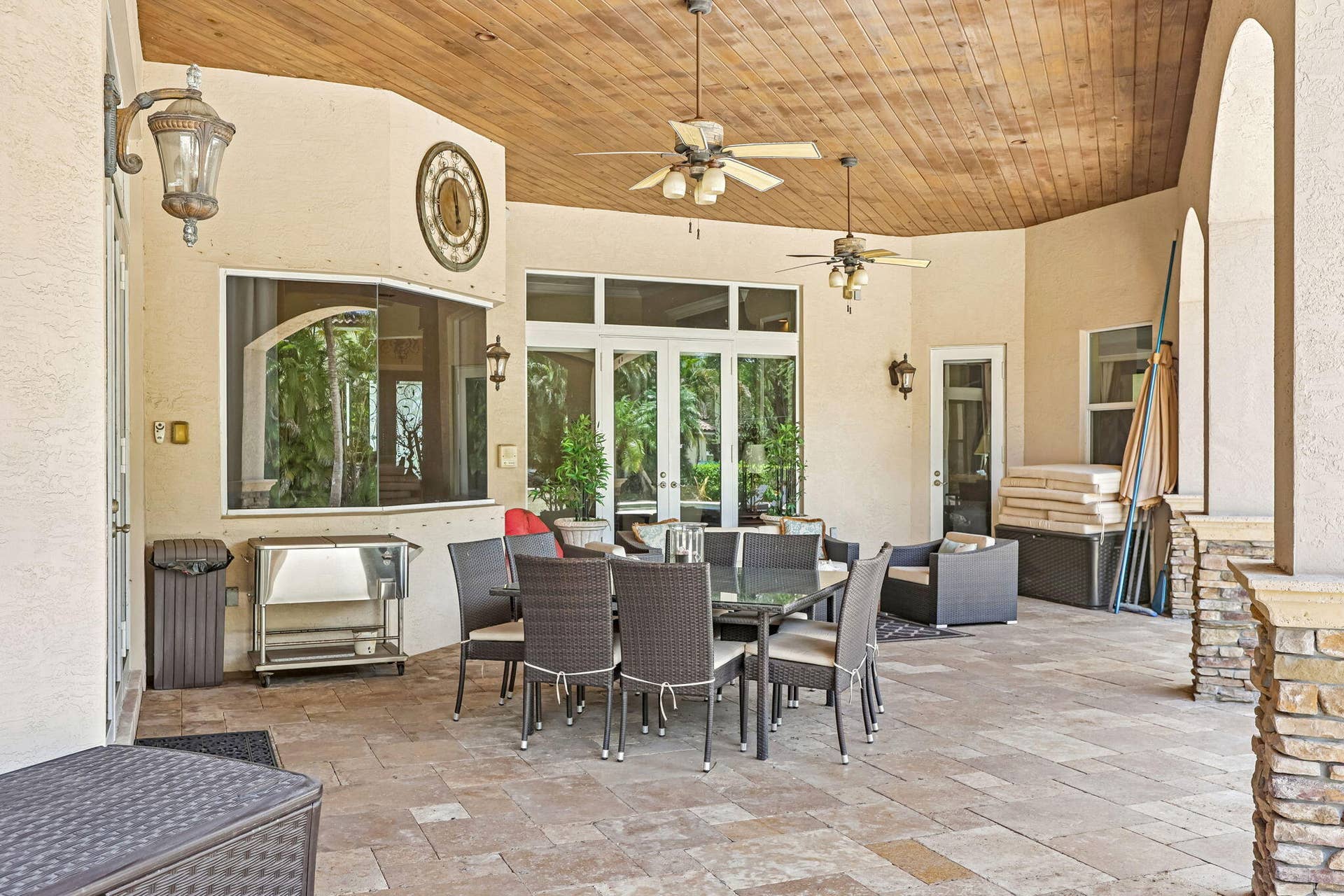 Expansive outdoor patio featuring a wood-finish ceiling, multiple ceiling fans, and sconce lighting