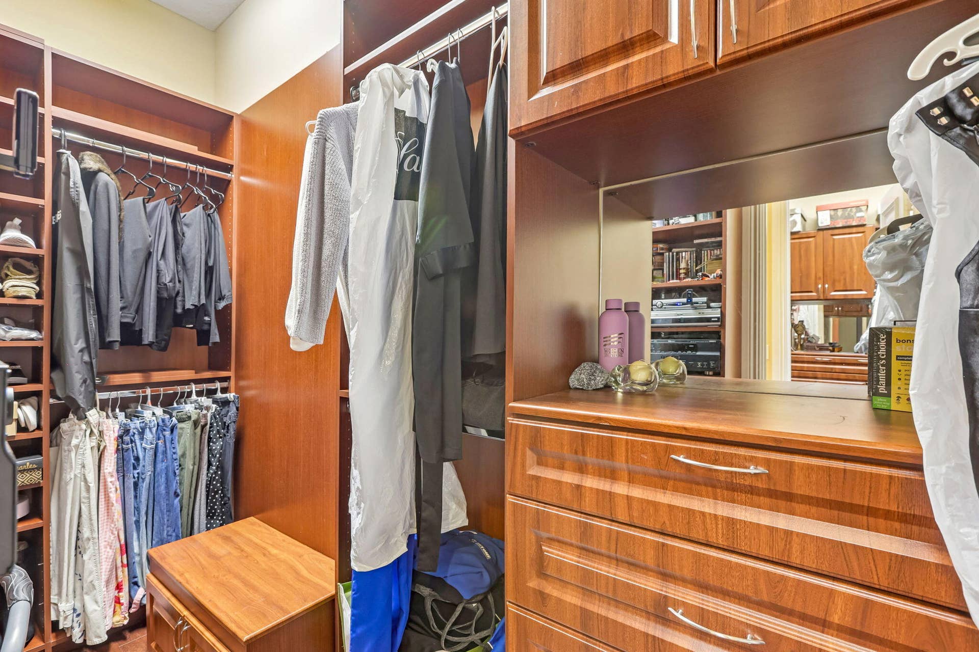 Expansive custom closet featuring warm wood-finish cabinetry, integrated shelving, multiple hanging rods, built-in drawers, and a recessed mirror
