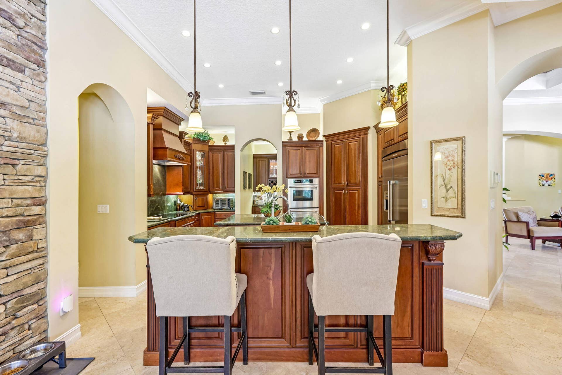 Gourmet kitchen featuring a large central island with seating, dark wood cabinetry, stainless steel appliances, recessed lighting, and green countertops