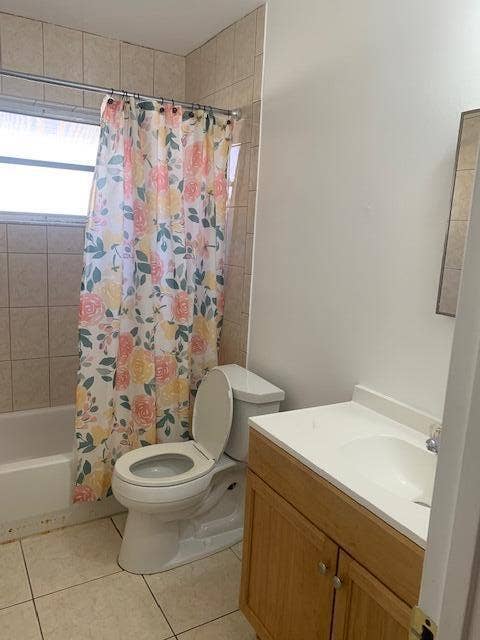 933 Francis Street, West Palm Beach, FL 33405 Bathroom featuring a white tub, light-toned wall tiling, a window, a white toilet, and a vanity with a light wood-finish cabinet and white countertop