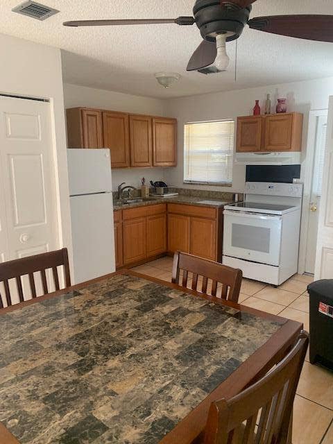 933 Francis Street, West Palm Beach, FL 33405 Kitchen featuring wood cabinetry, white appliances, and light-toned tile flooring