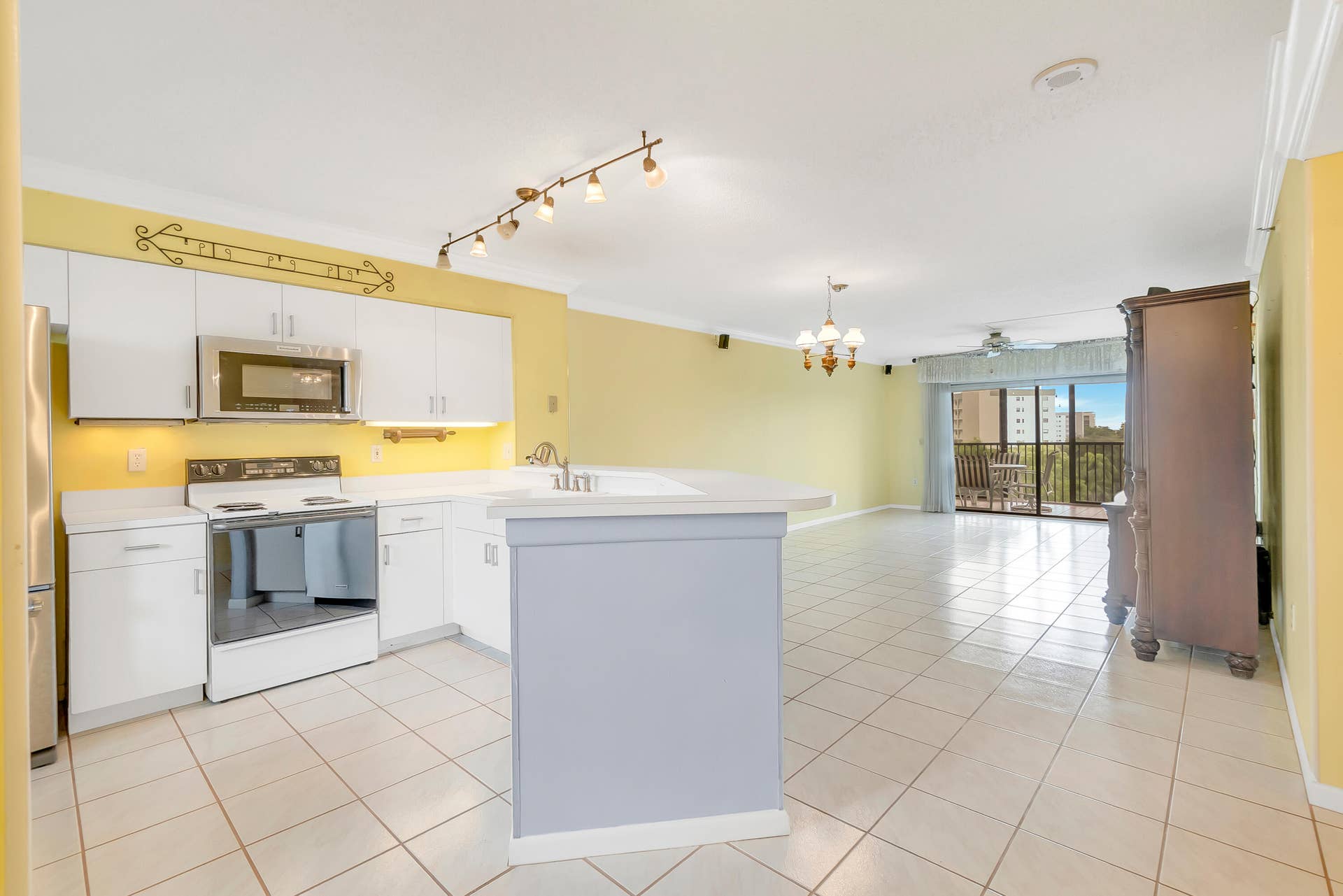 2334 S Cypress Bend Drive, #602, Pompano Beach, FL 33069 Open-concept living area with tile flooring throughout, featuring a kitchen with white cabinetry, stainless steel appliances, and a breakfast bar.