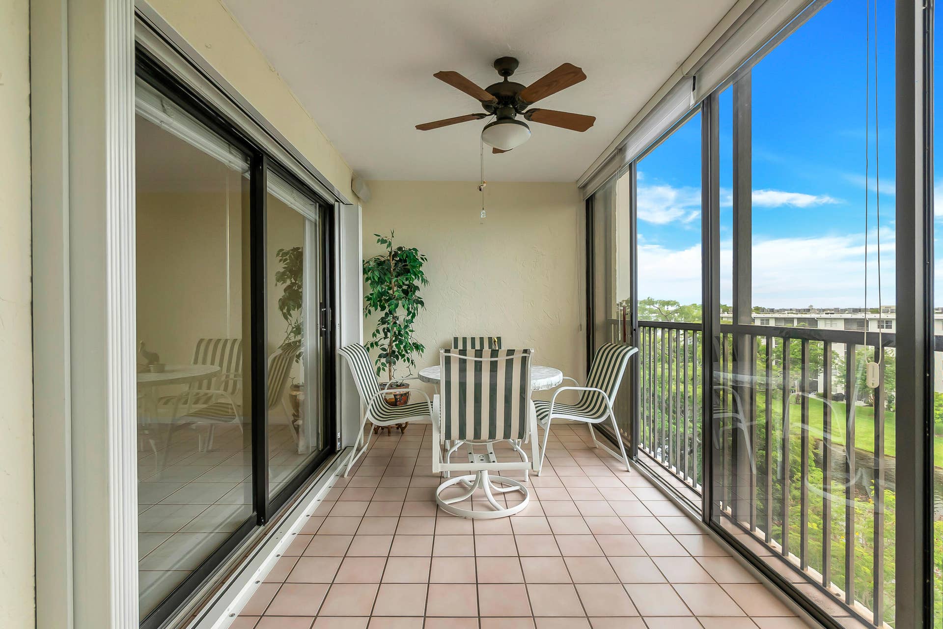 2334 S Cypress Bend Drive, #602, Pompano Beach, FL 33069 Enclosed balcony featuring light-toned tile flooring, a ceiling fan with integrated lighting, and expansive sliding glass panels offering substantial natural light. Full accordion hurricane shutters