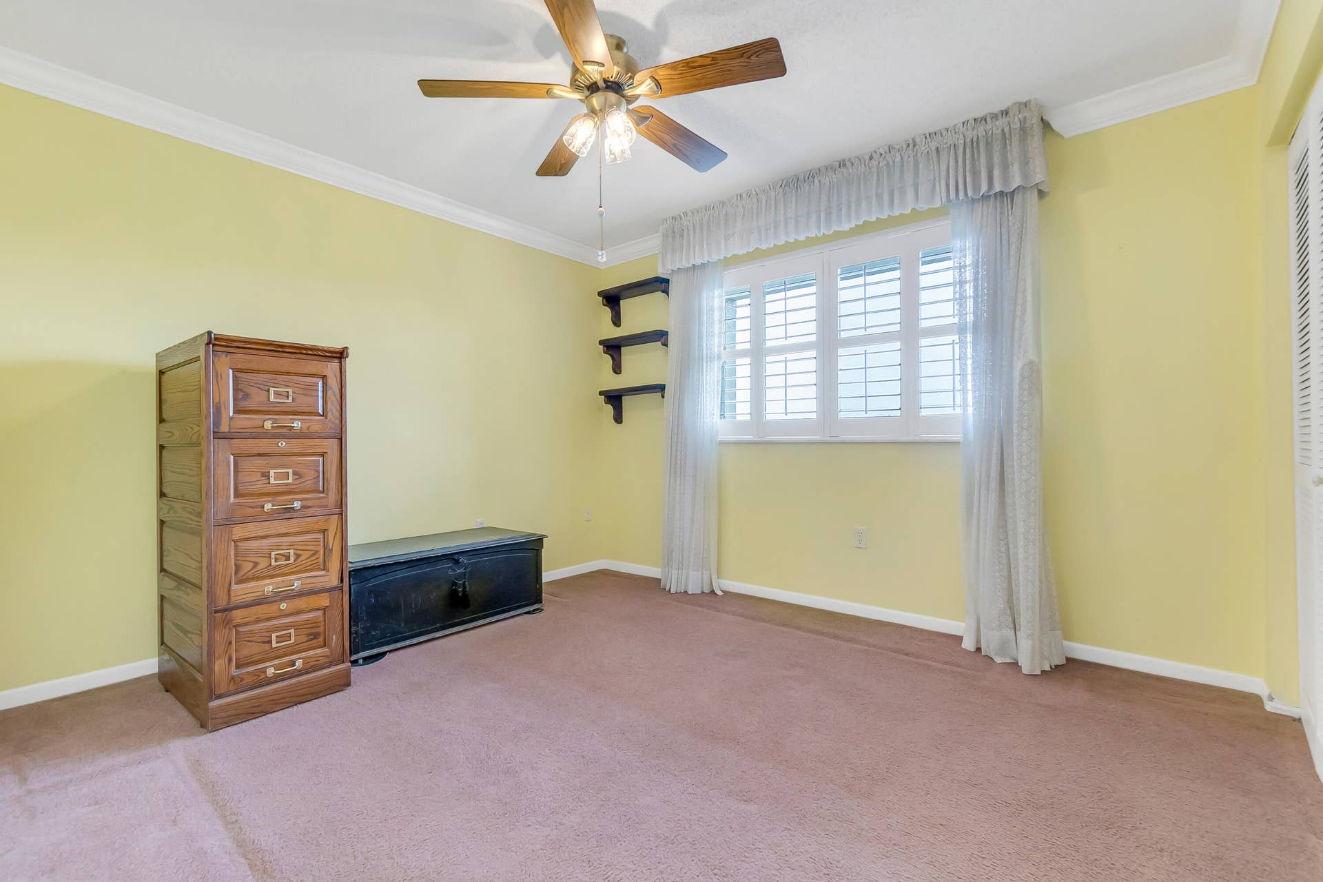 2334 S Cypress Bend Drive, #602, Pompano Beach, FL 33069 Carpeted room with a ceiling fan light fixture, crown molding, and a window featuring white plantation shutters and sheer lace curtains