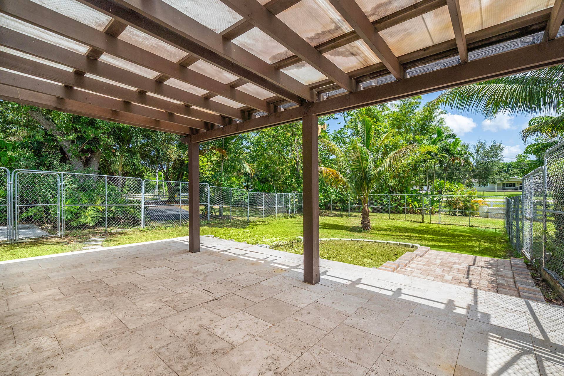 4950 Thoroughbred Lane, Southwest Ranches, FL 33330 Covered side patio with square stone tile flooring, a wood-frame pergola, and a translucent roof