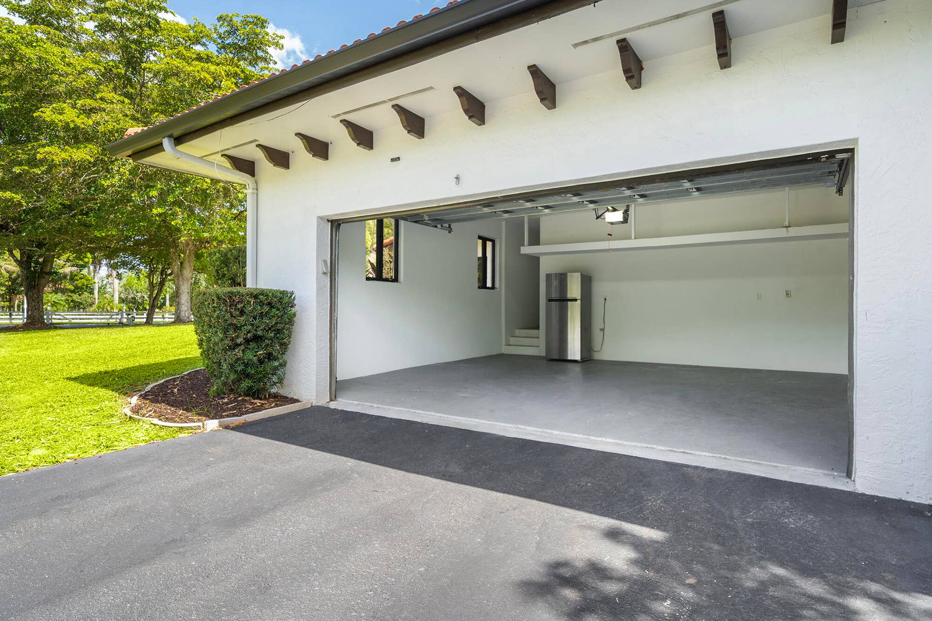 4950 Thoroughbred Lane, Southwest Ranches, FL 33330 Attached garage with a paved driveway, featuring a concrete floor, white interior walls, and a visible window