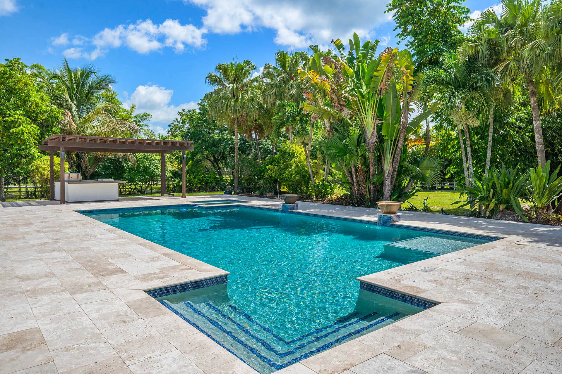 4950 Thoroughbred Lane, Southwest Ranches, FL 33330 Resort-style pool area featuring a rectangular pool with integrated steps, neutral-toned travertine marble paver decking, and a separate spa