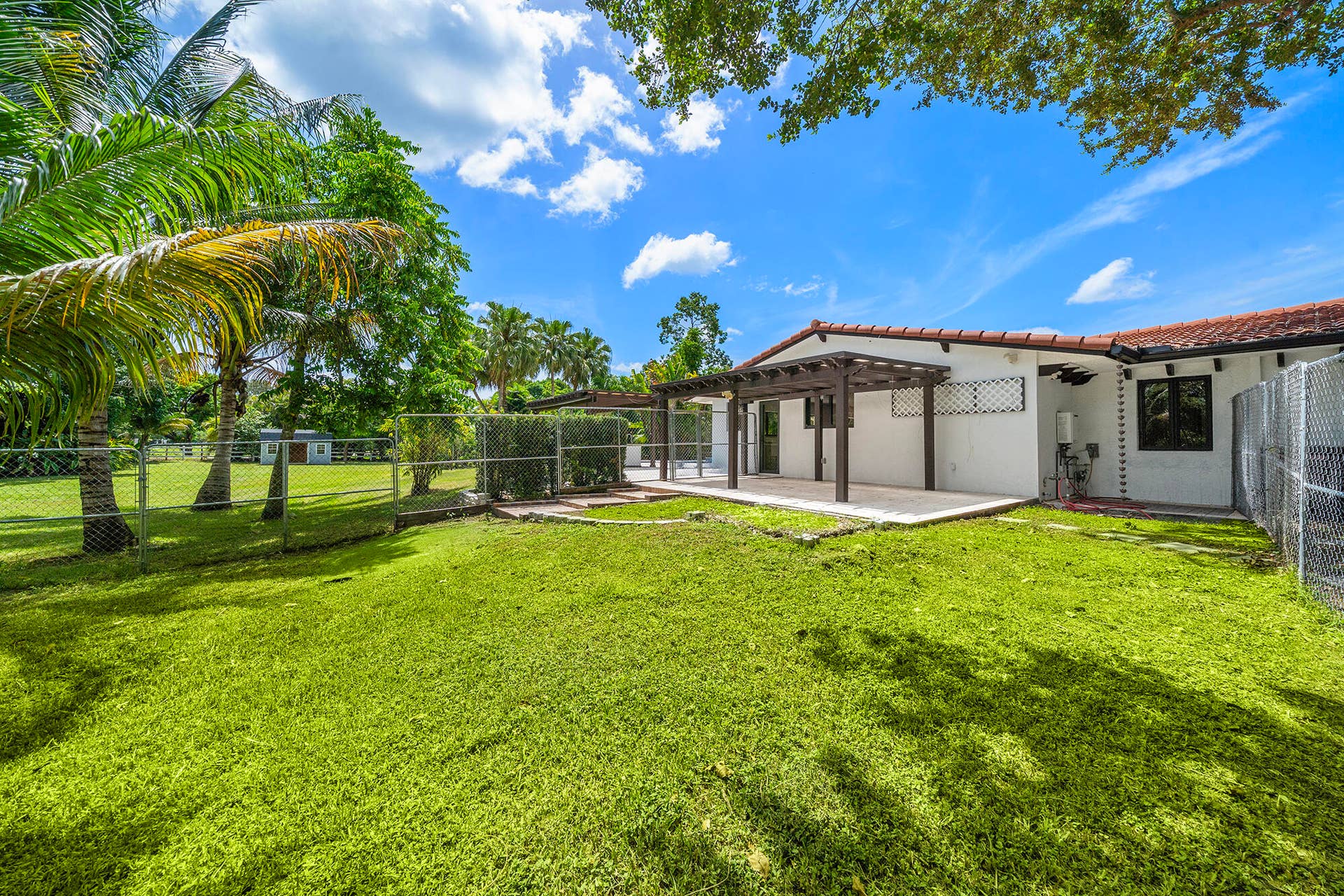 4950 Thoroughbred Lane, Southwest Ranches, FL 33330 Expansive sideyard featuring a lush lawn, mature palm trees, and perimeter chain-link fencing