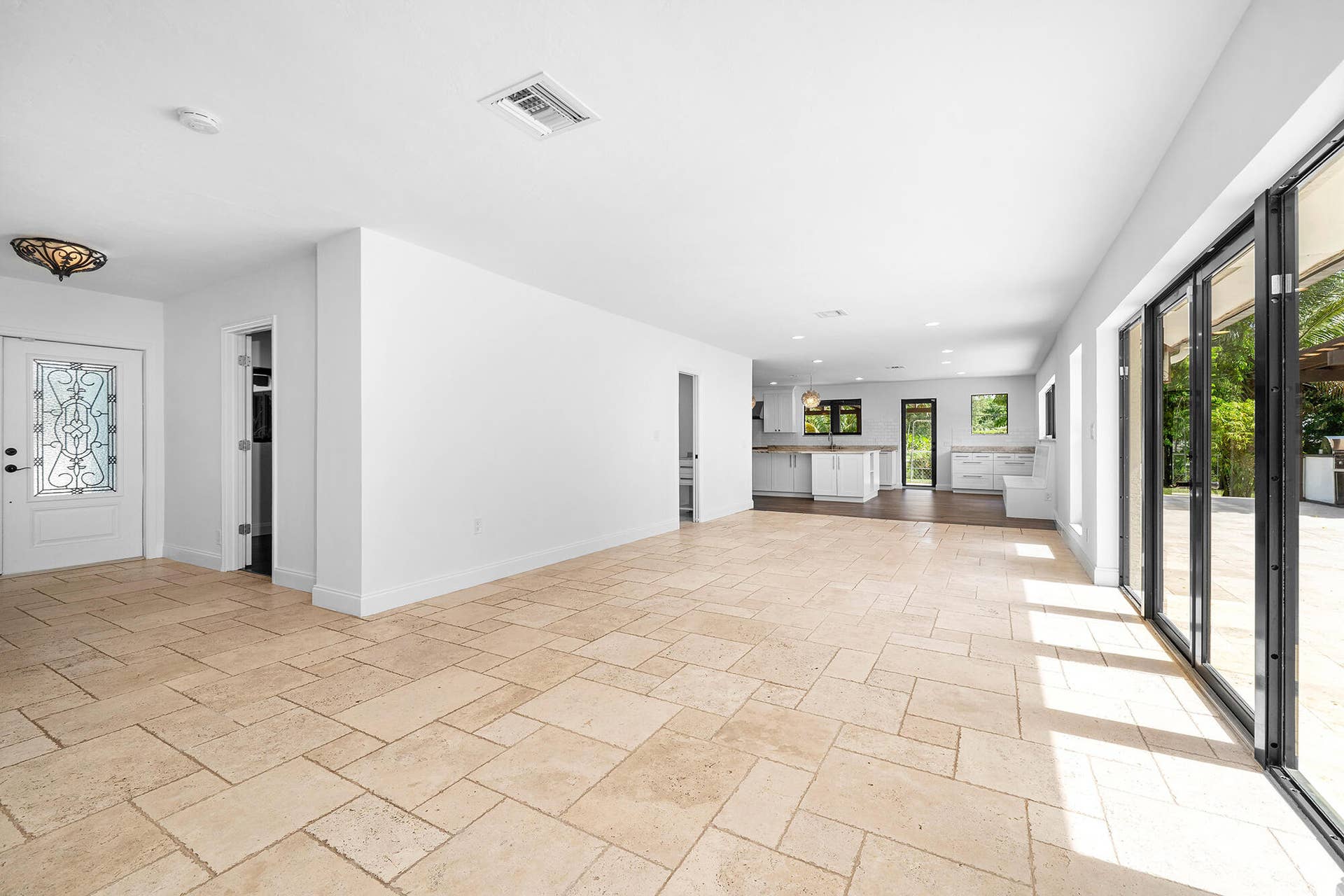 4950 Thoroughbred Lane, Southwest Ranches, FL 33330 Spacious room featuring light-toned tile flooring, a decorative entry door with leaded glass, and a modern folding glass door system opening to an exterior patio