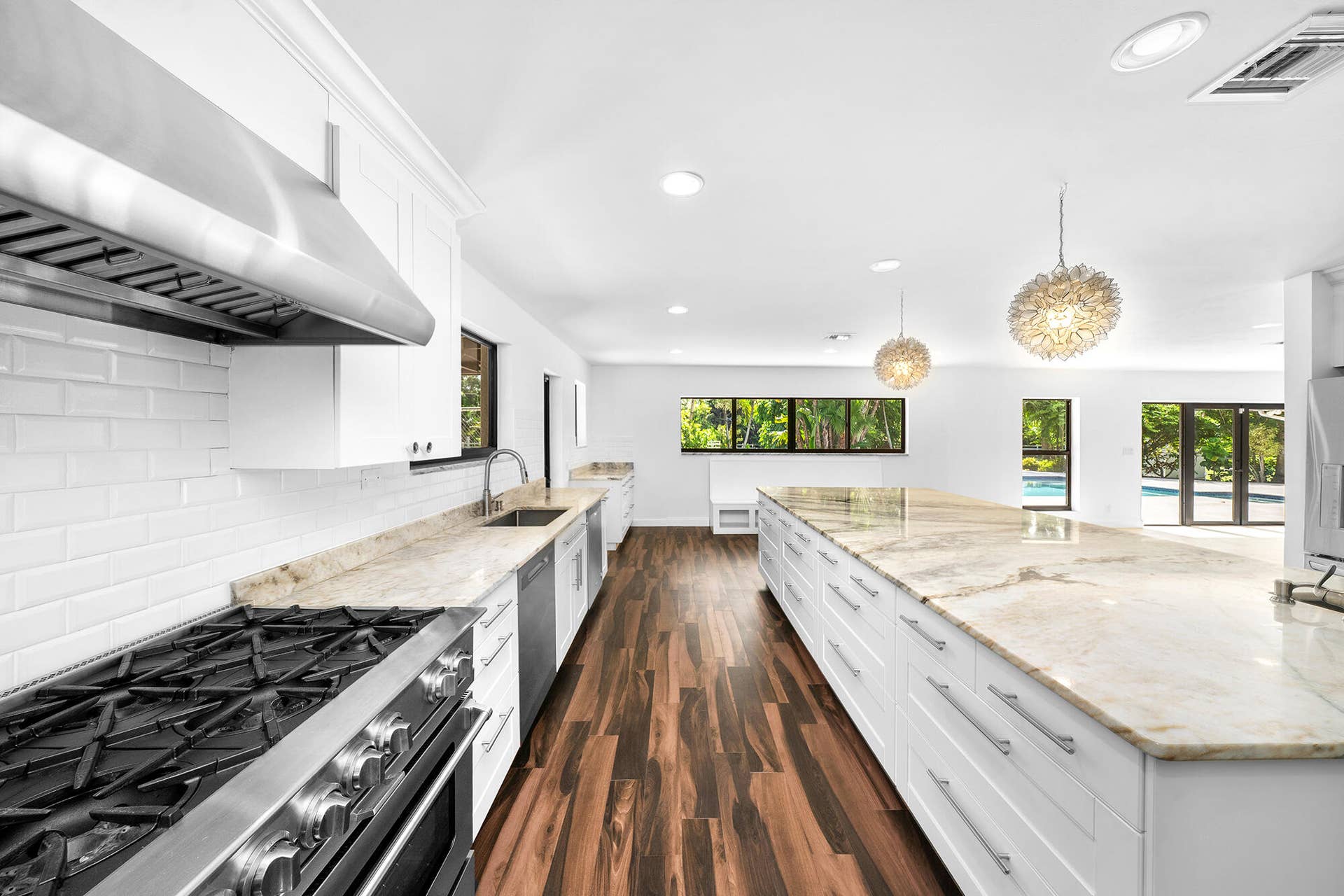 4950 Thoroughbred Lane, Southwest Ranches, FL 33330 Expansive kitchen featuring a large central island with stone countertop, wood-finish flooring, white cabinetry, stainless steel range with hood, and modern pendant lighting