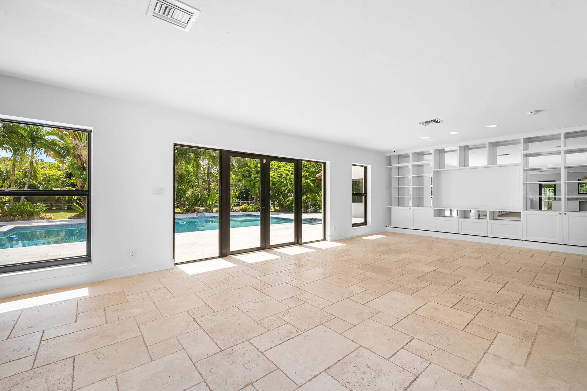 4950 Thoroughbred Lane, Southwest Ranches, FL 33330 Spacious living area featuring and travertine marble flooring, extensive built-in shelving, recessed lighting, and multiple large windows with sliding glass doors opening to a private outdoor pool