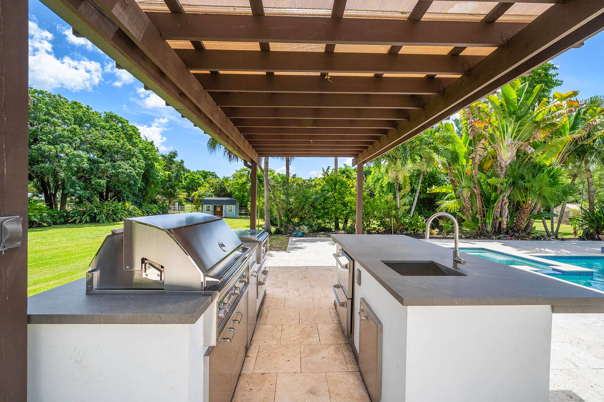 4950 Thoroughbred Lane, Southwest Ranches, FL 33330 Outdoor kitchen featuring a built-in grill, integrated sink with faucet, and under-counter refrigeration, all beneath a wood pergola