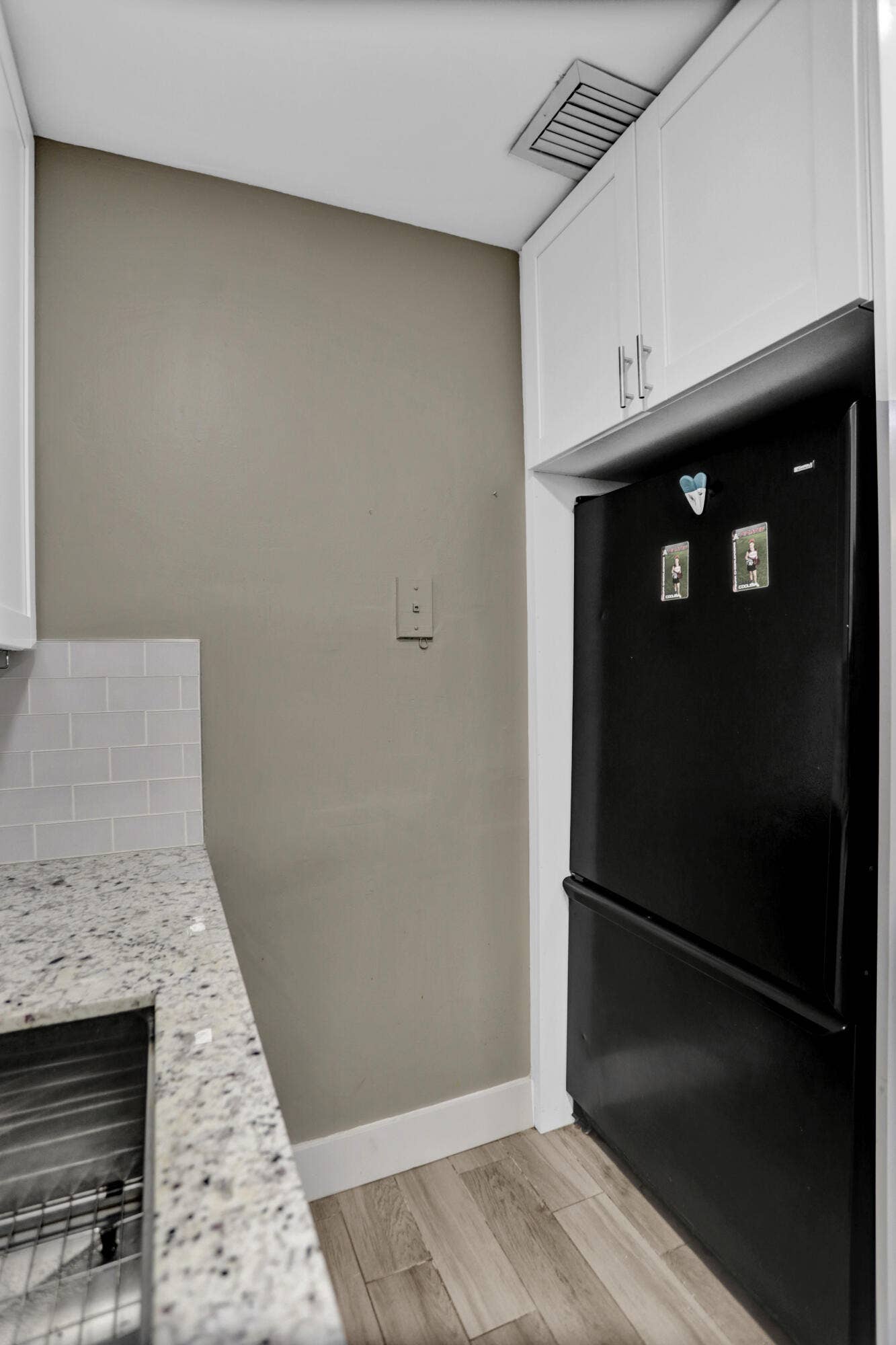 Updated kitchen featuring white shaker cabinetry, speckled countertop, tile backsplash, stainless steel sink, and wood-finish flooring