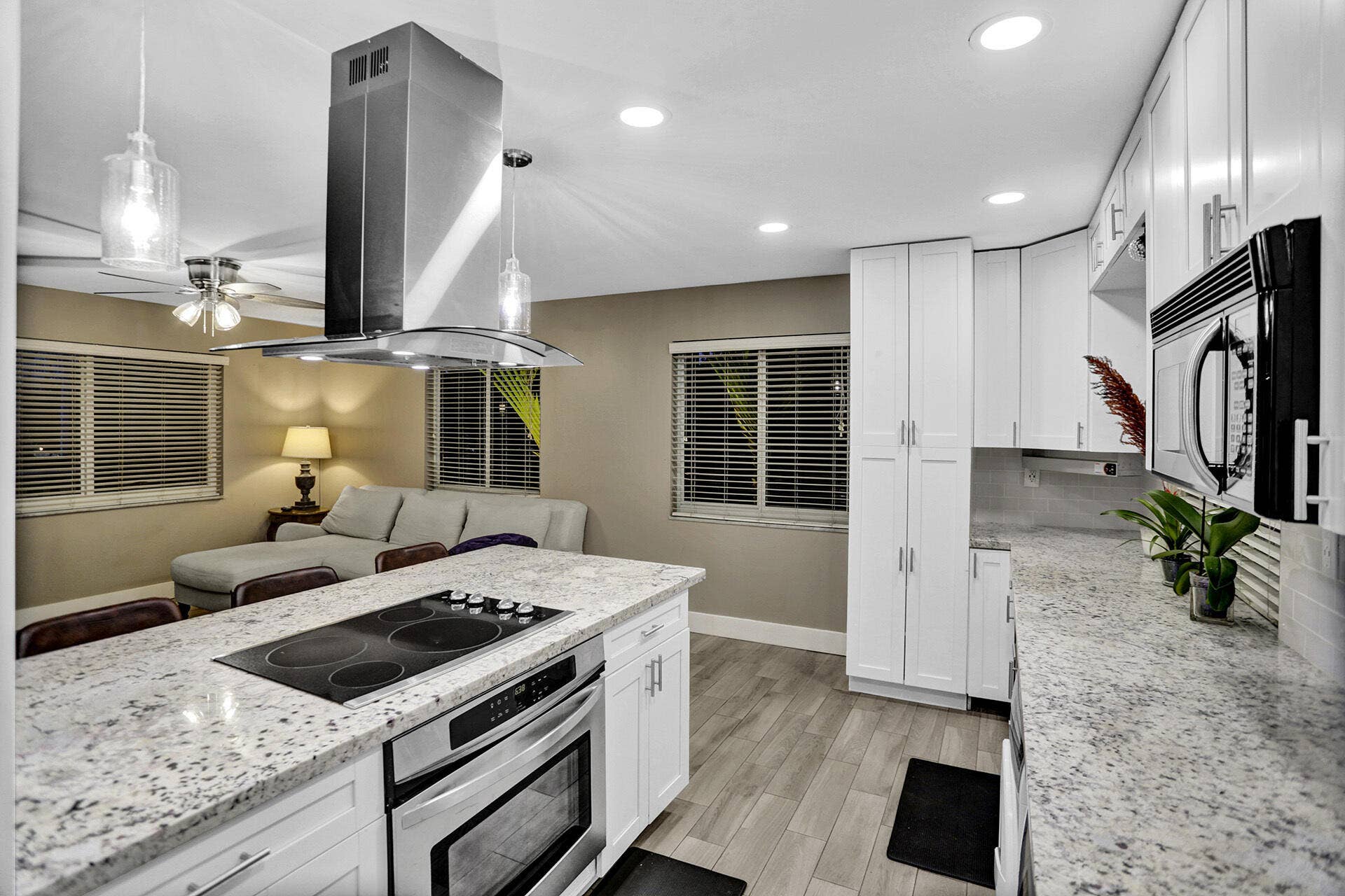Open-concept kitchen featuring an island with an integrated cooktop and stainless steel oven, white cabinetry, speckled countertops, and recessed lighting