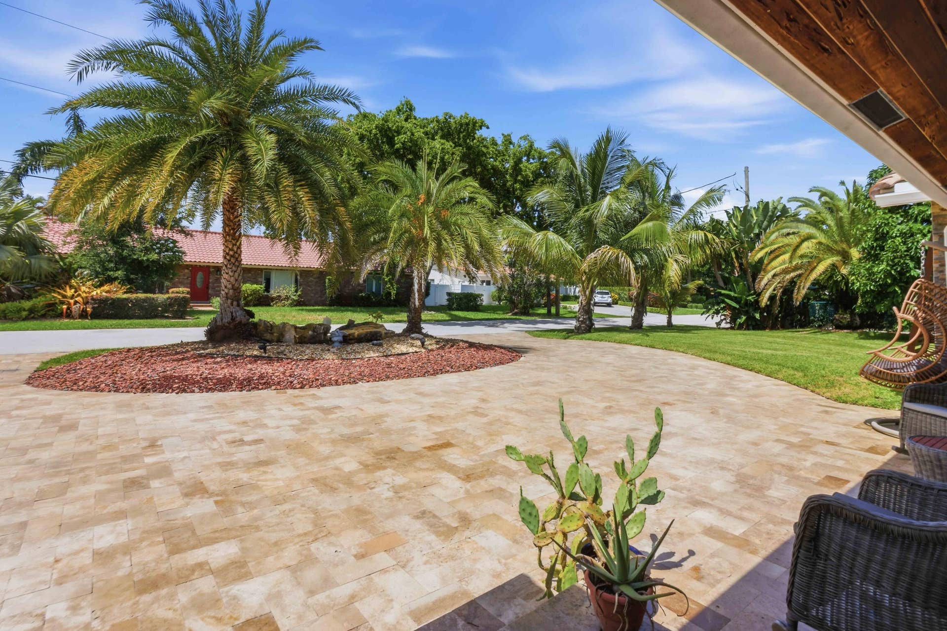 3316 NE 40TH Court, Fort Lauderdale, FL 33308 Expansive paver driveway with a central landscaped island featuring mature palm trees and decorative rock