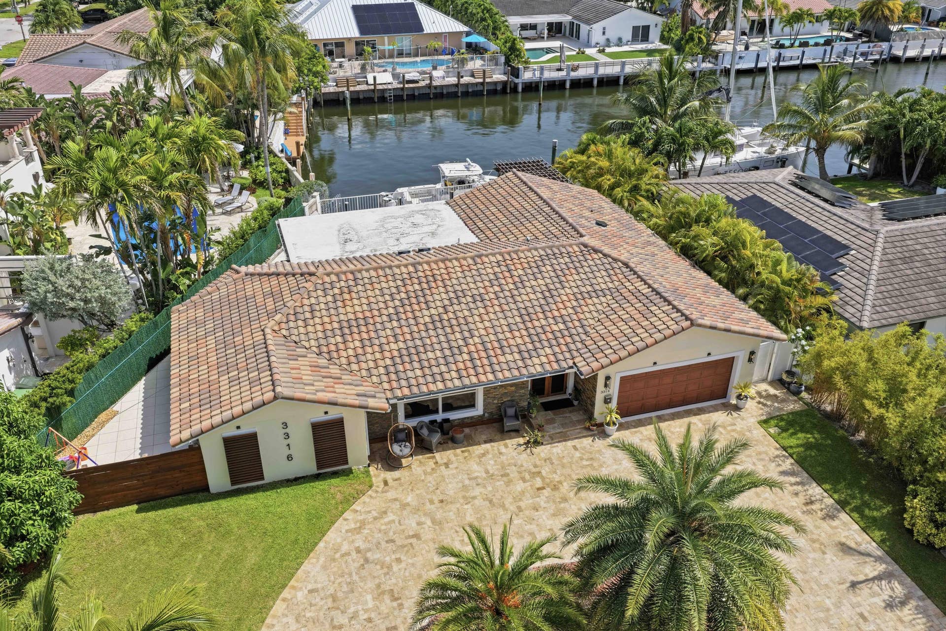 3316 NE 40TH Court, Fort Lauderdale, FL 33308 Waterfront residence featuring a paver driveway, terracotta-style roof, mature palm trees, and a two-car garage with a wood-finish door