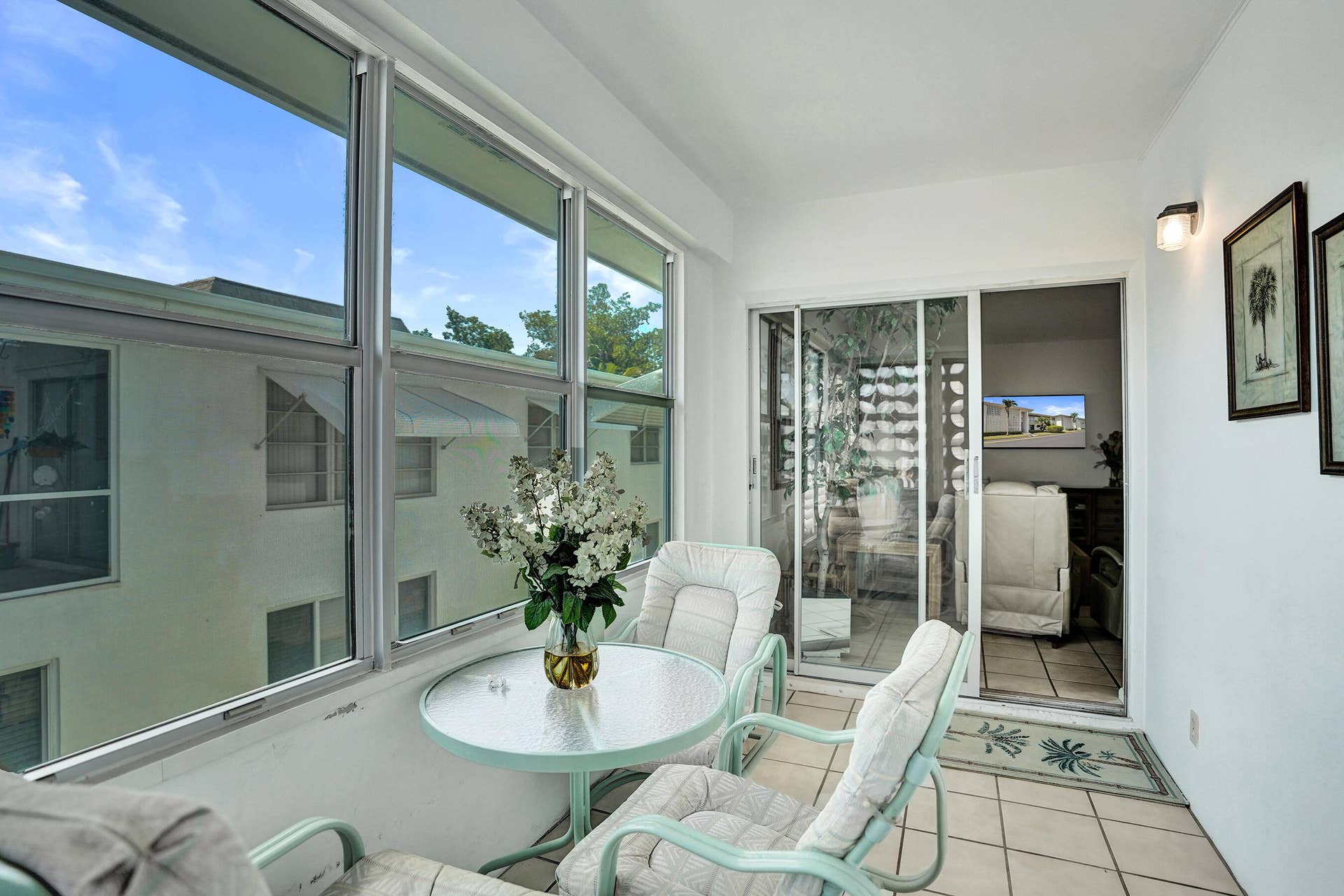 Enclosed patio featuring wall-to-wall windows, sliding glass door, white tile flooring, and a wall-mounted sconce