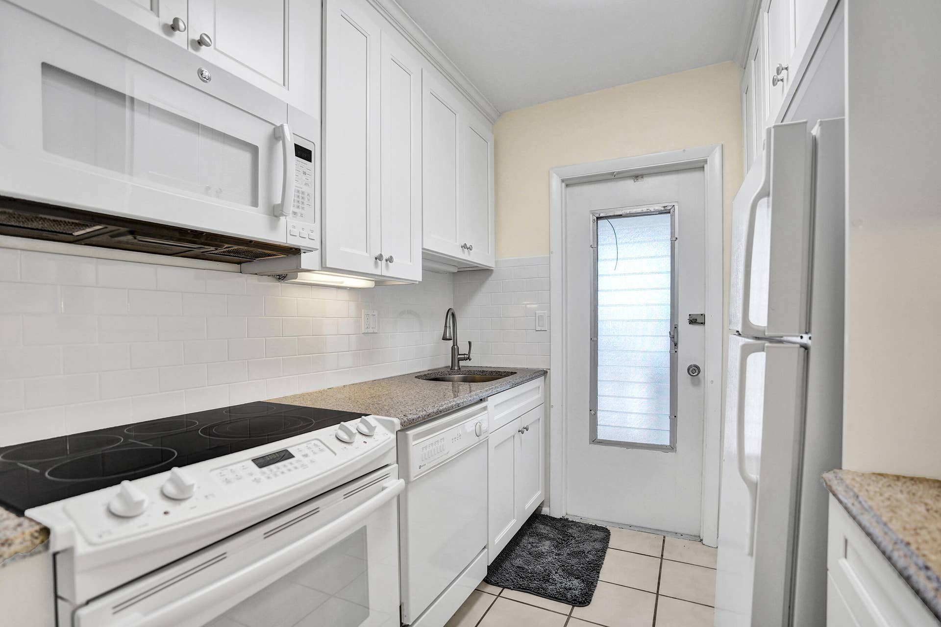 Kitchen featuring white cabinetry with silver hardware, speckled countertops, and a white subway tile backsplash