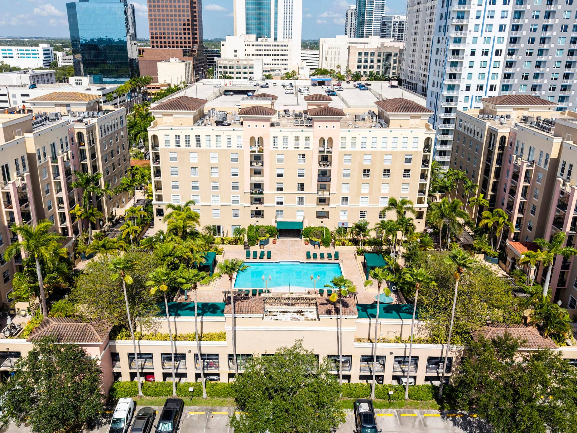 Resort-style pool deck featuring a heated pool, spa, outdoor TVs, bar, showers, and lush tropical landscaping.