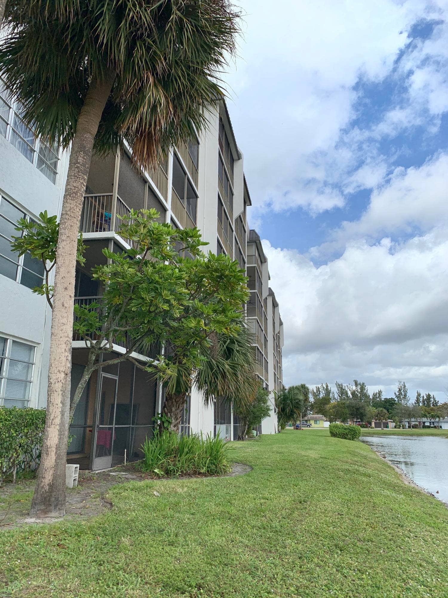 3100 W Rolling Hills Circle, #309, Davie, Davie, FL 33328 Multi-story building featuring screened balconies and patios, mature palm trees, manicured lawn, and waterside frontage