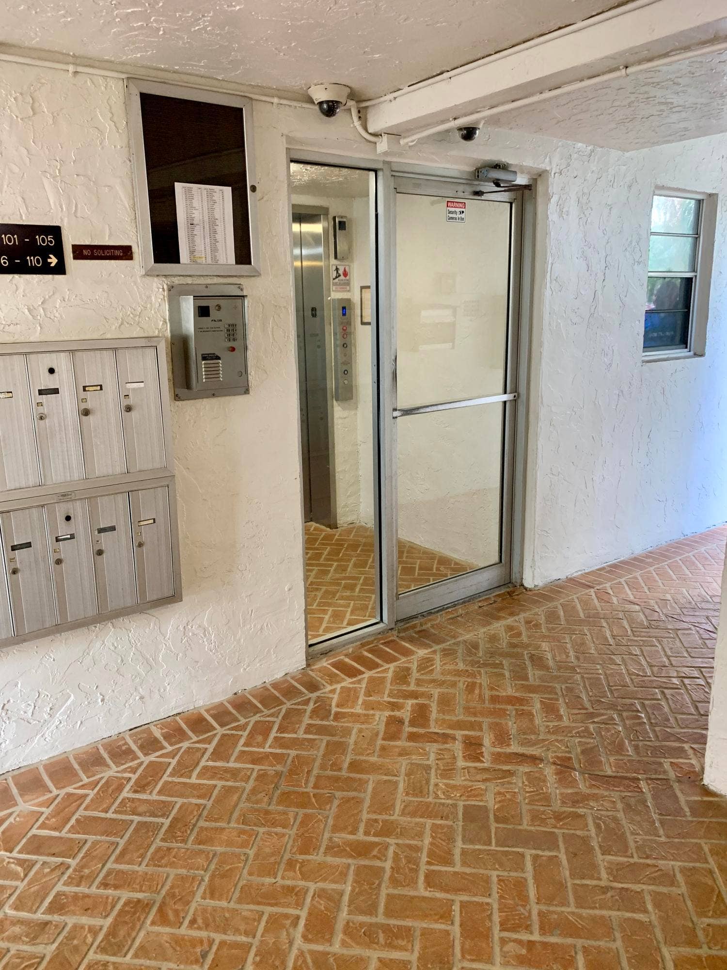 3100 W Rolling Hills Circle, #309, Davie, Davie, FL 33328 Entryway featuring a herringbone brick floor pattern, white stucco walls, and a glass-paneled entry door