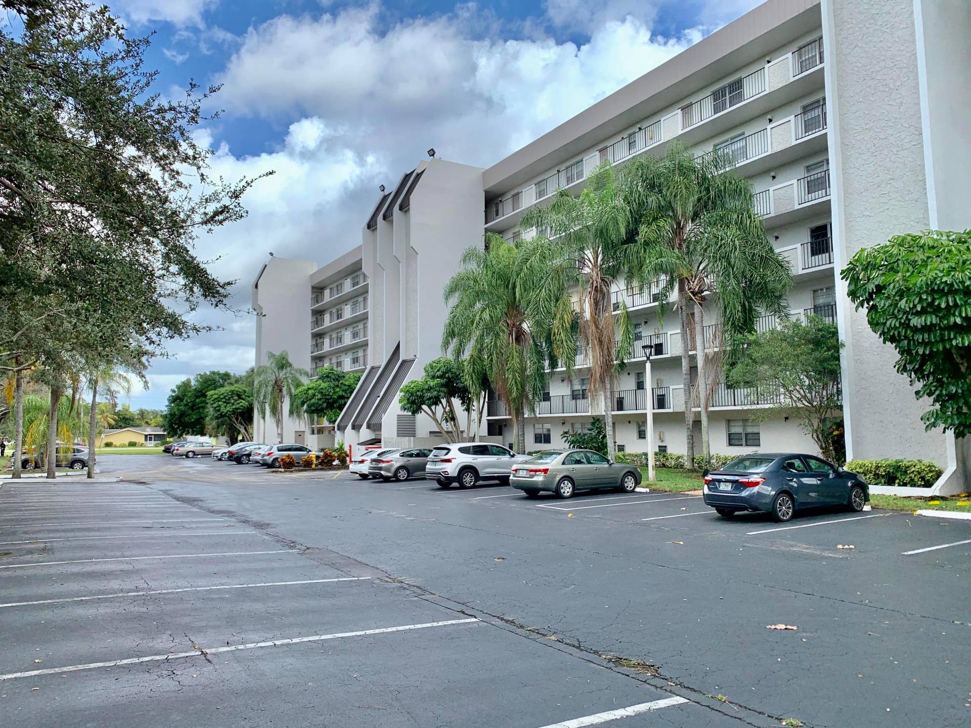 3100 W Rolling Hills Circle, #309, Davie, Davie, FL 33328 Multi-story residential building featuring private balconies with white railings, mature palm trees, and ample paved parking